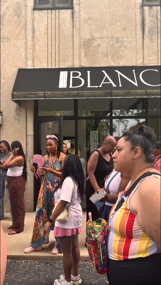 Group of people standing and waiting outside a store called 'BLANC'.