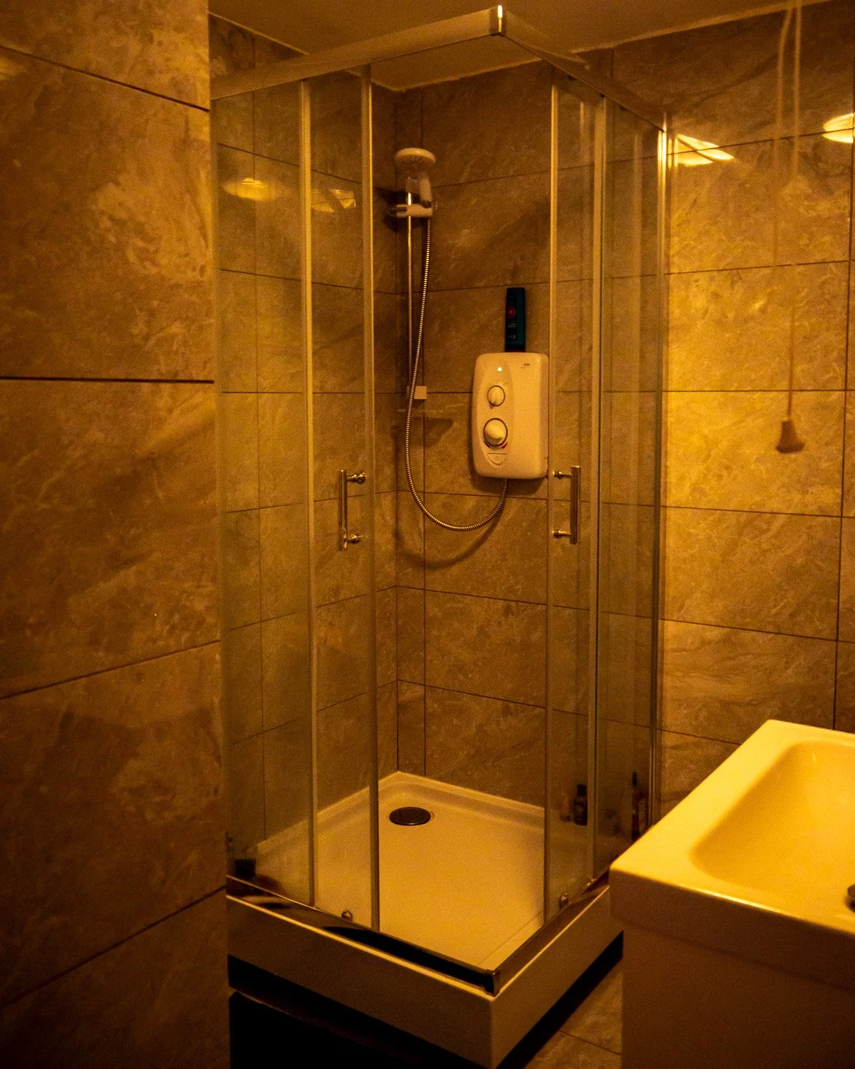 Small enclosed shower with tiled walls and a white electric water heater mounted on the wall inside the shower.
