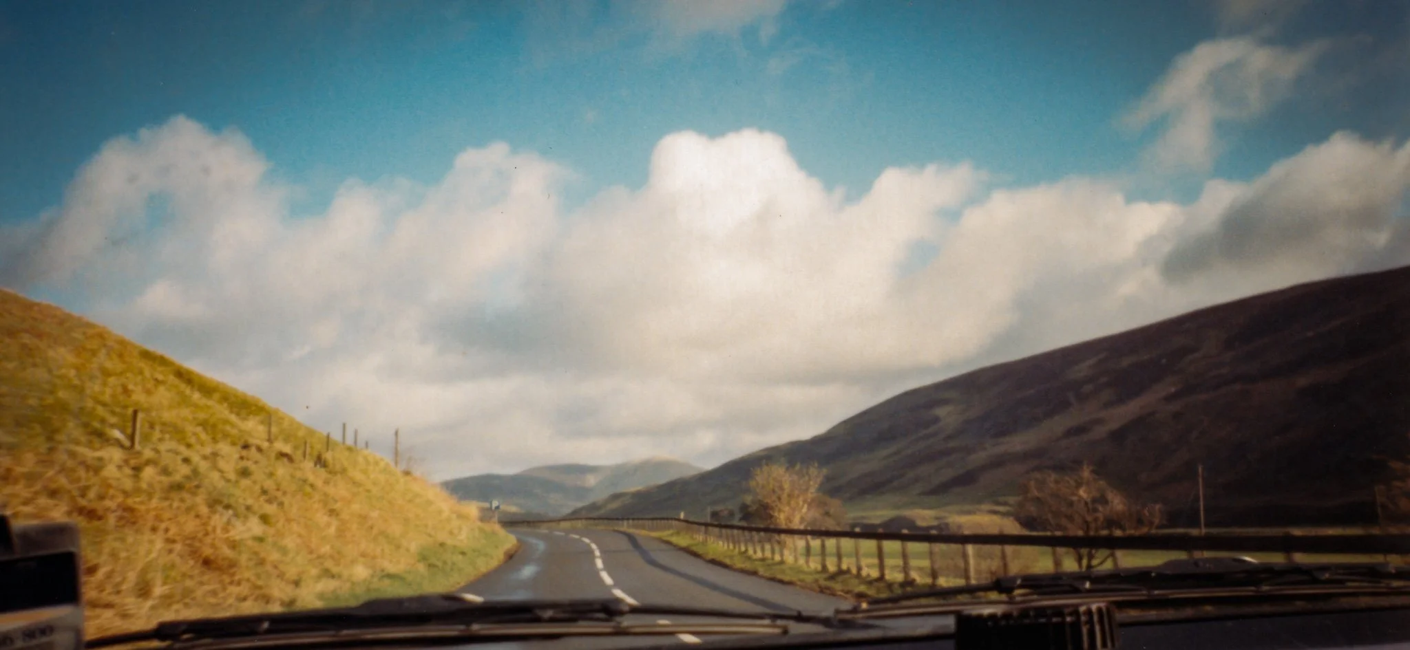 A scenic view of a winding road through rolling hills under a partly cloudy sky.