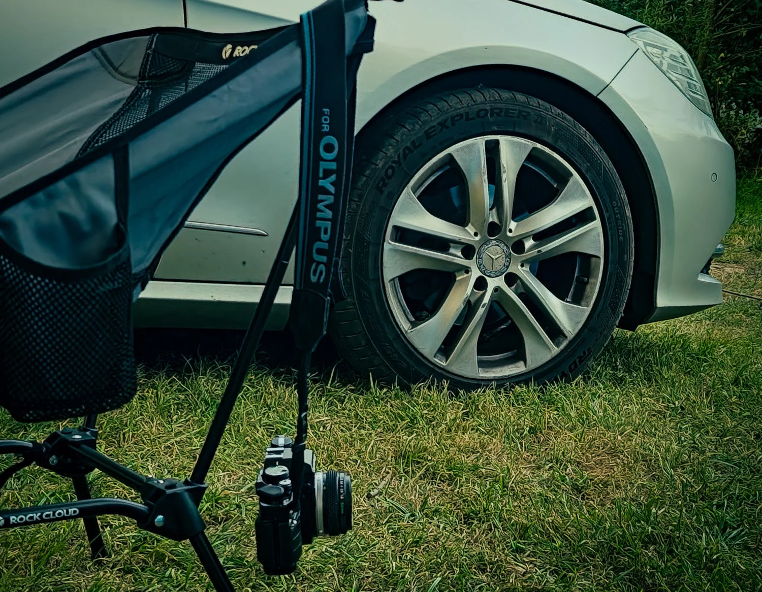 A white Mercedes-Benz car parked on grass, partially visible, with a golf bag and a golf trolley in the foreground.