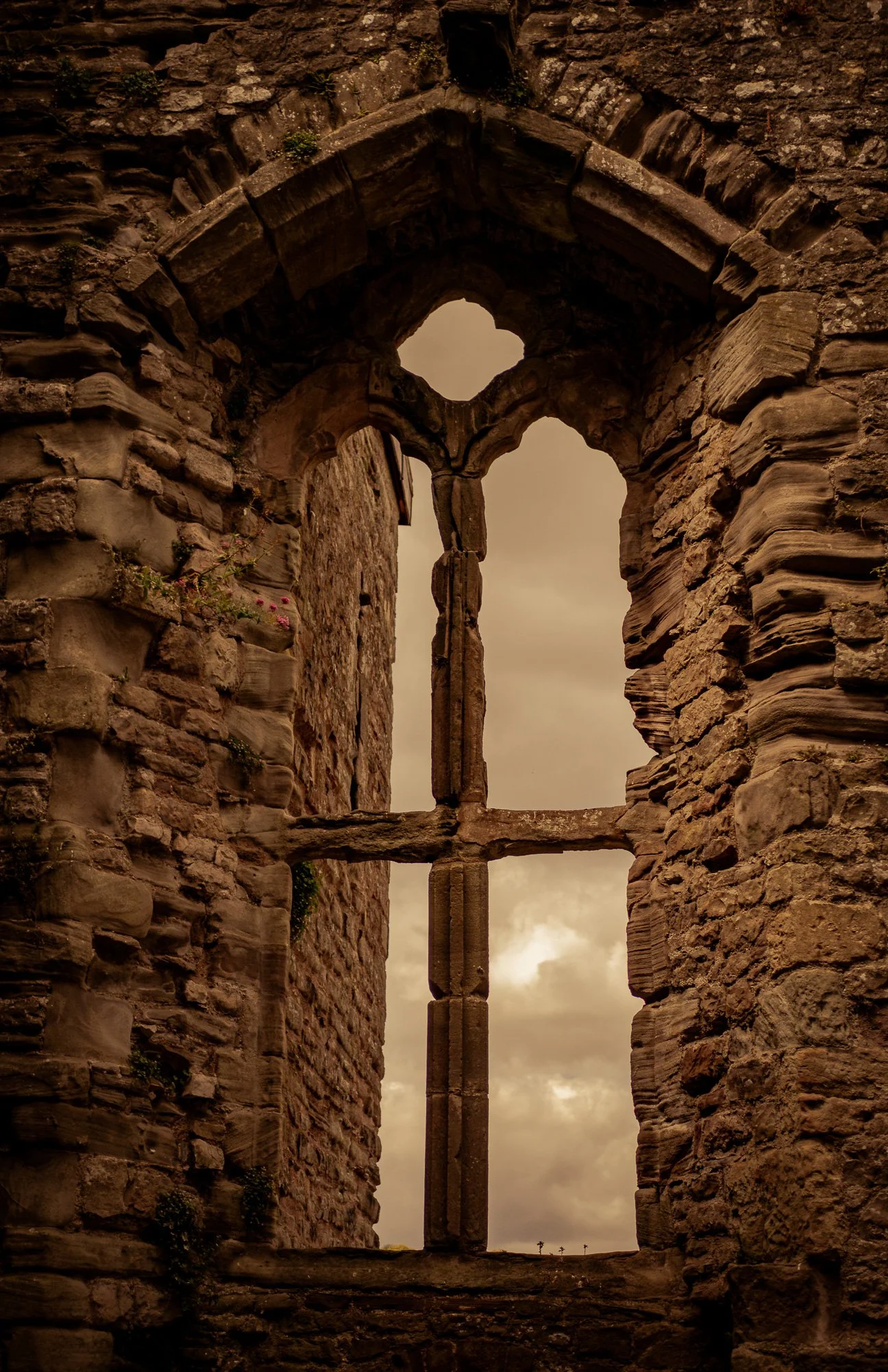 The image shows the remaining walls of an old stone building with a pointed arch window, through which a cloudy sky is visible.
