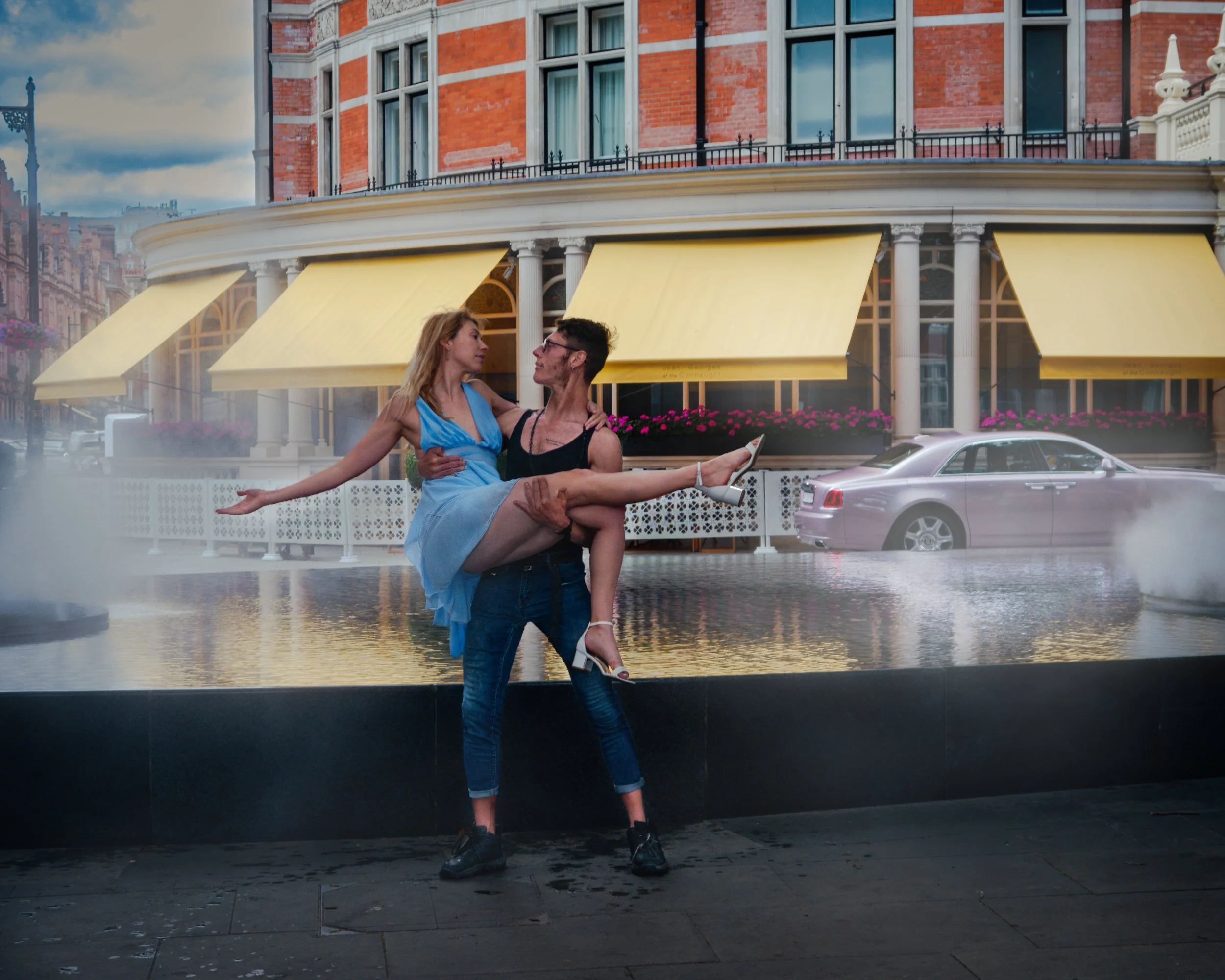 A man holding a woman in a scene that appears to be digitally altered or staged, in front of a building with yellow awnings and a city street background, including cars and brick buildings.