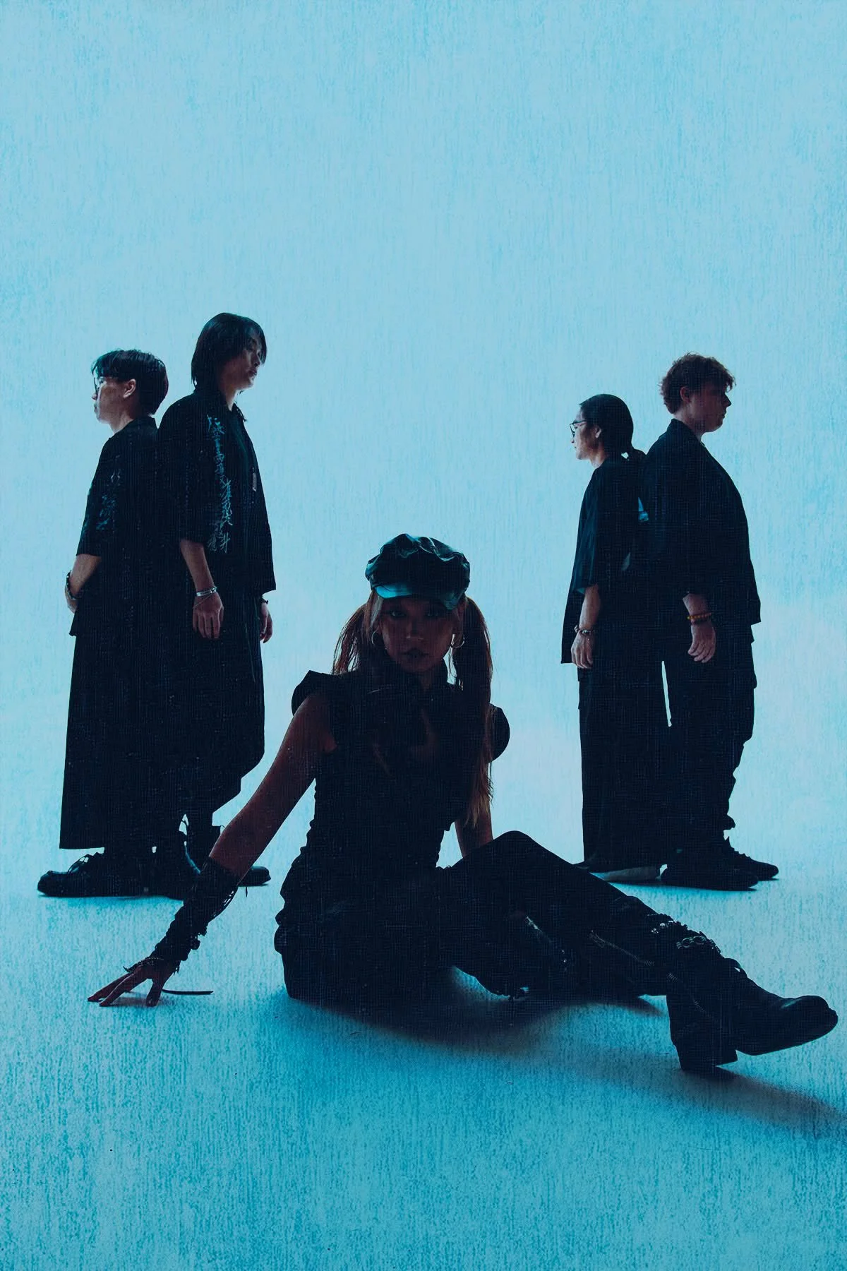 A group of five people, all members of P.H.0, one sitting on the ground and four standing, all dressed in dark clothing, with a minimalistic bright blue background.