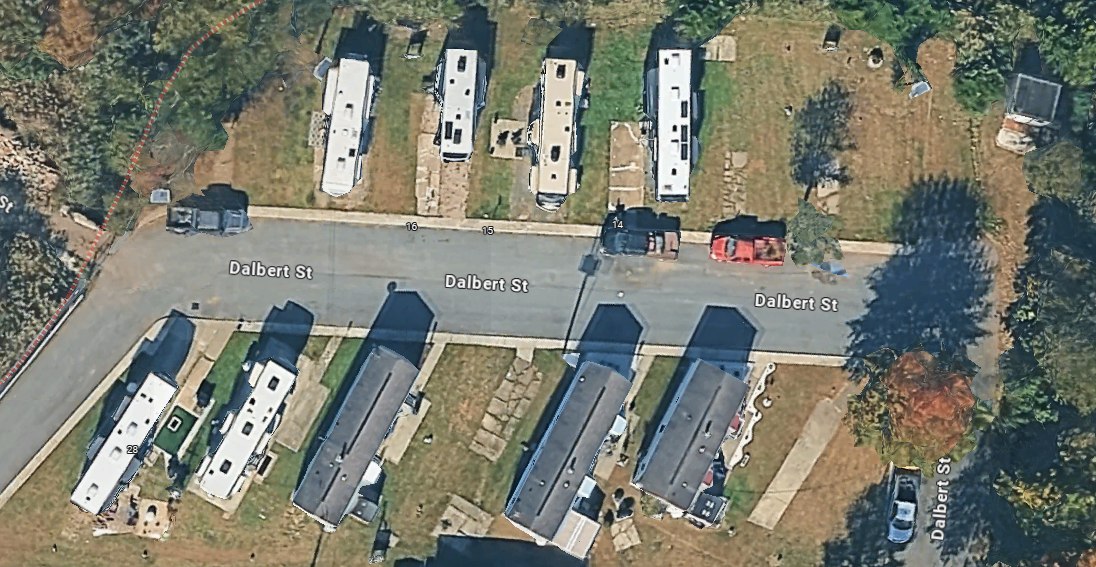 An aerial view of a residential street named Dalbert Street with several houses and parked cars, surrounded by trees.