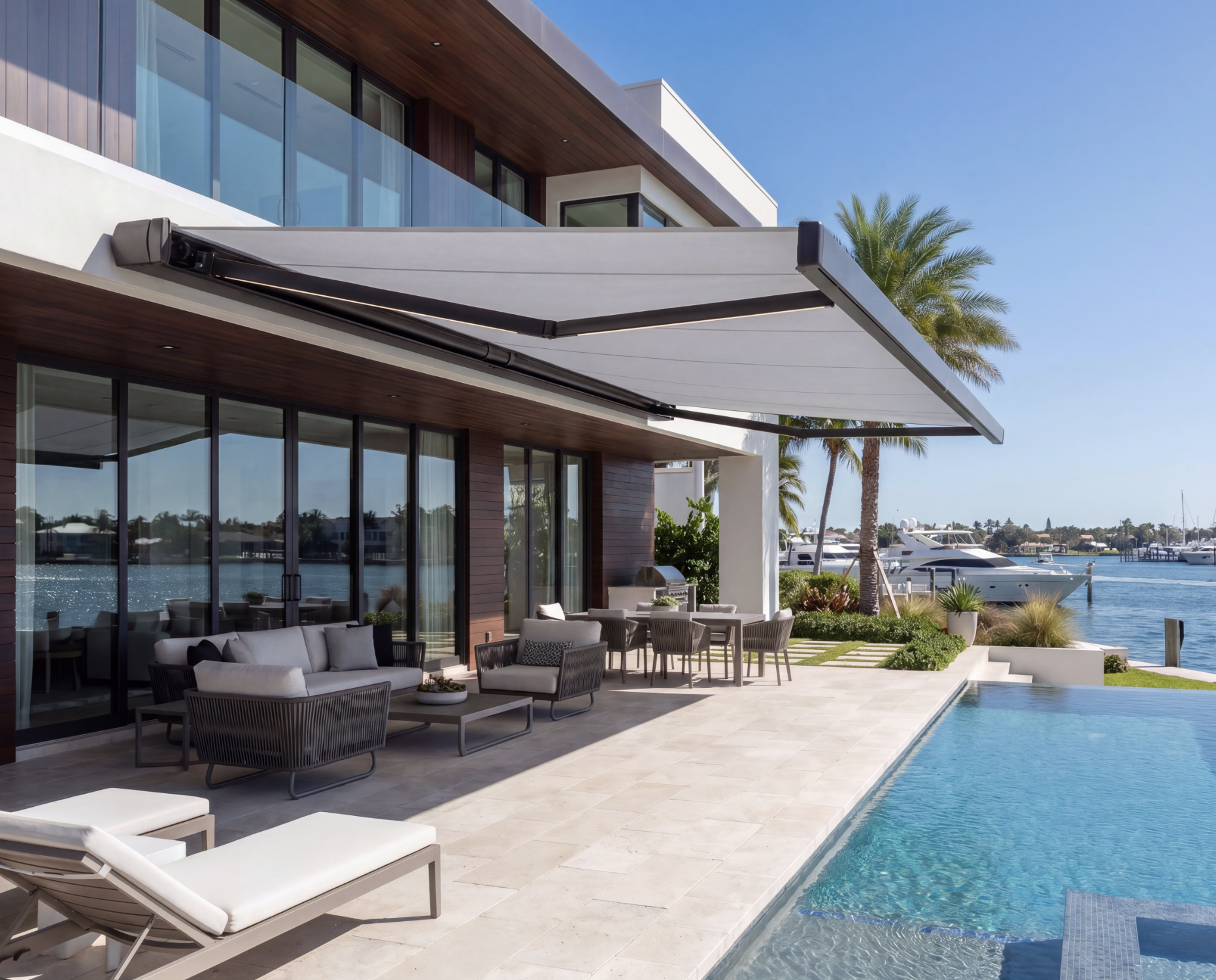 Luxury waterfront house with patio, outdoor seating, pool, and boats docked at marina, palm trees, and clear blue sky