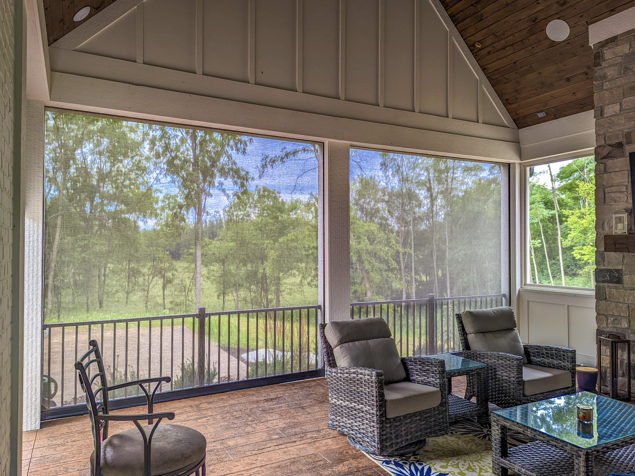A screened porch with wicker furniture, a glass-top table, and a view of trees outside.