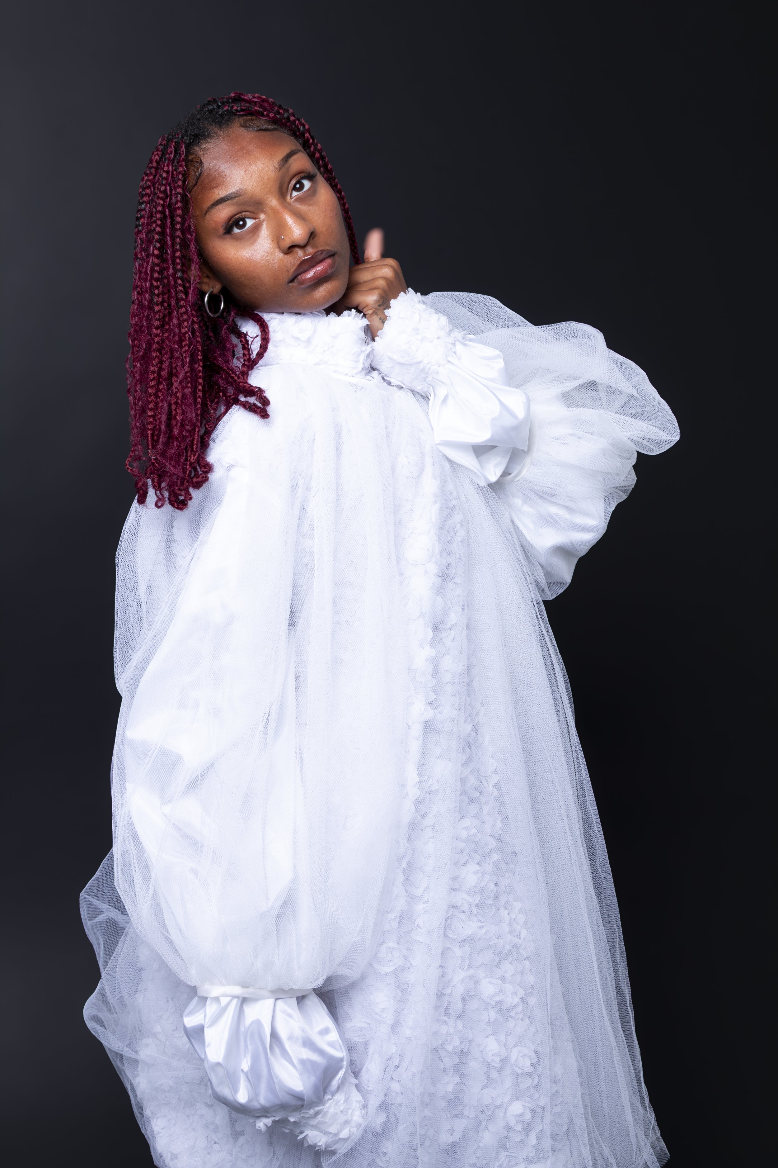 Young woman with red braids in a white dress with puffed sleeves, posing against a dark background.