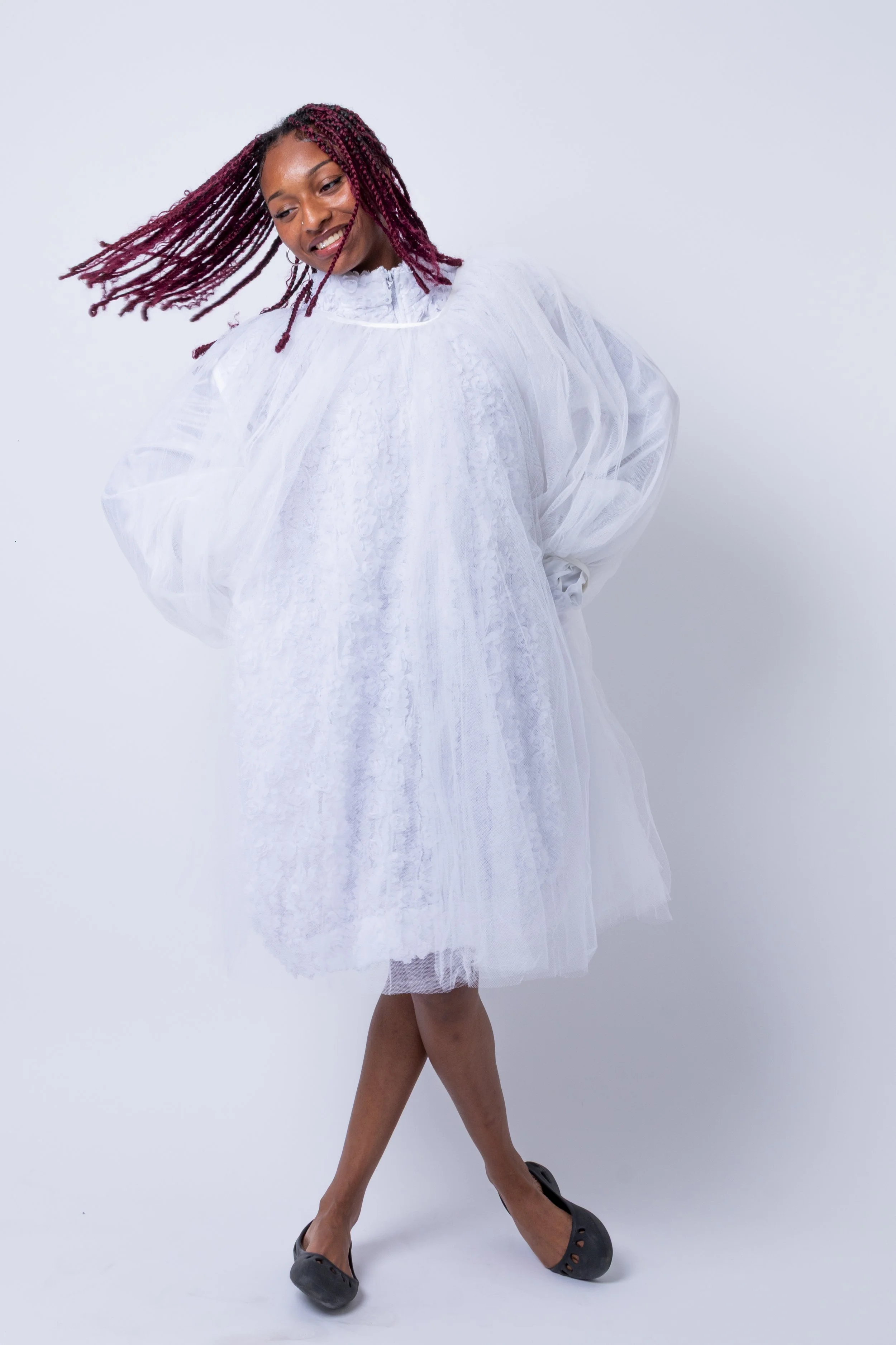Woman in white tulle dress in a dance pose, wearing black ballet flats, against a plain white background.