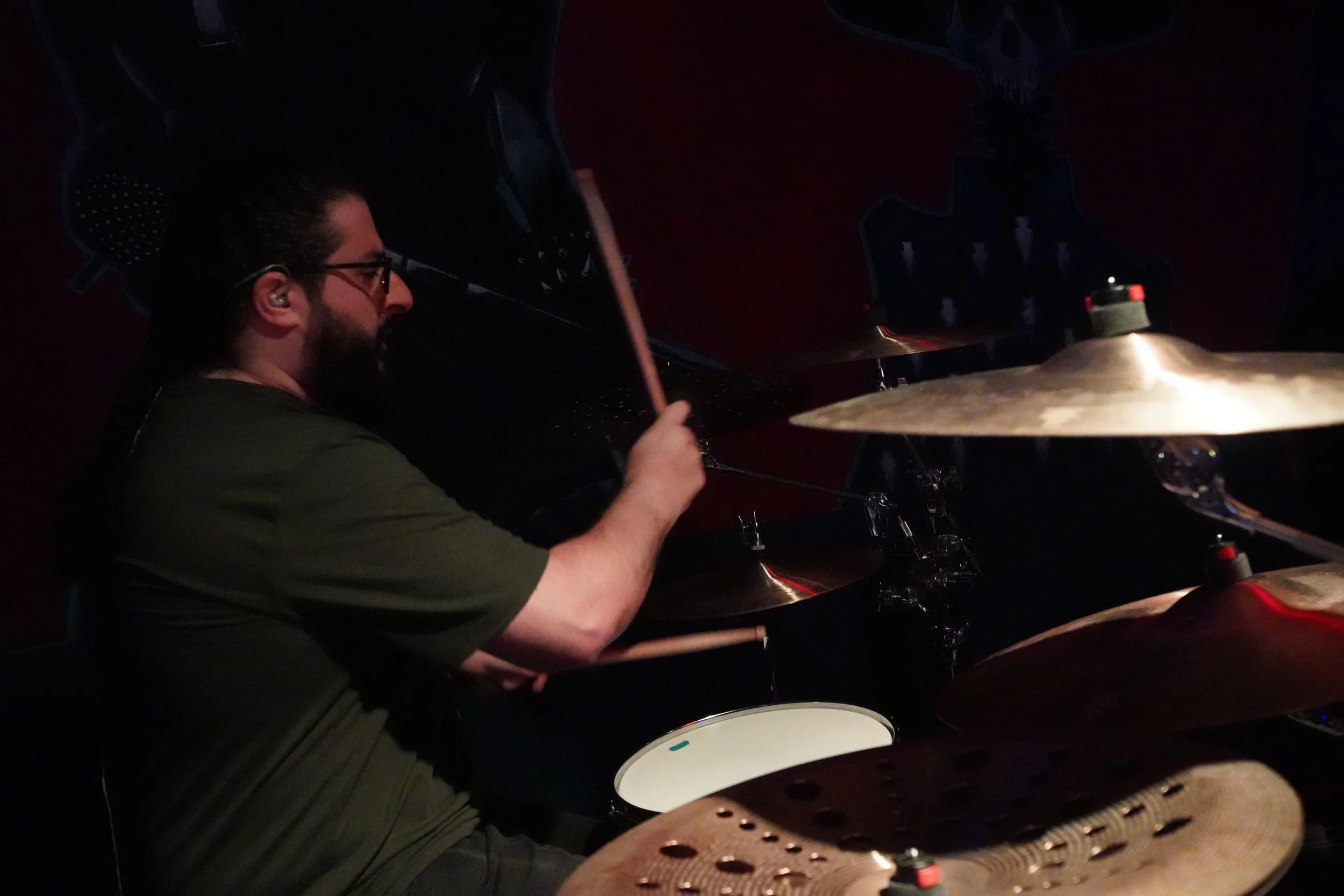 A man with glasses and a beard playing drums in a dimly lit setting.