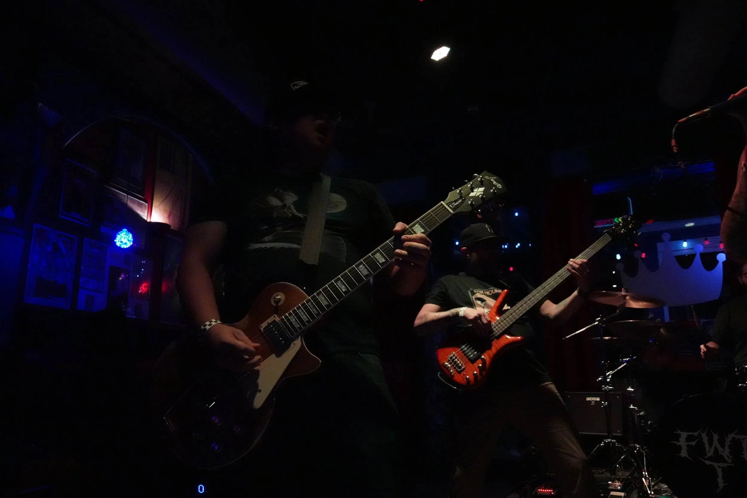 Dark image of musicians playing guitars on stage with dim lighting.