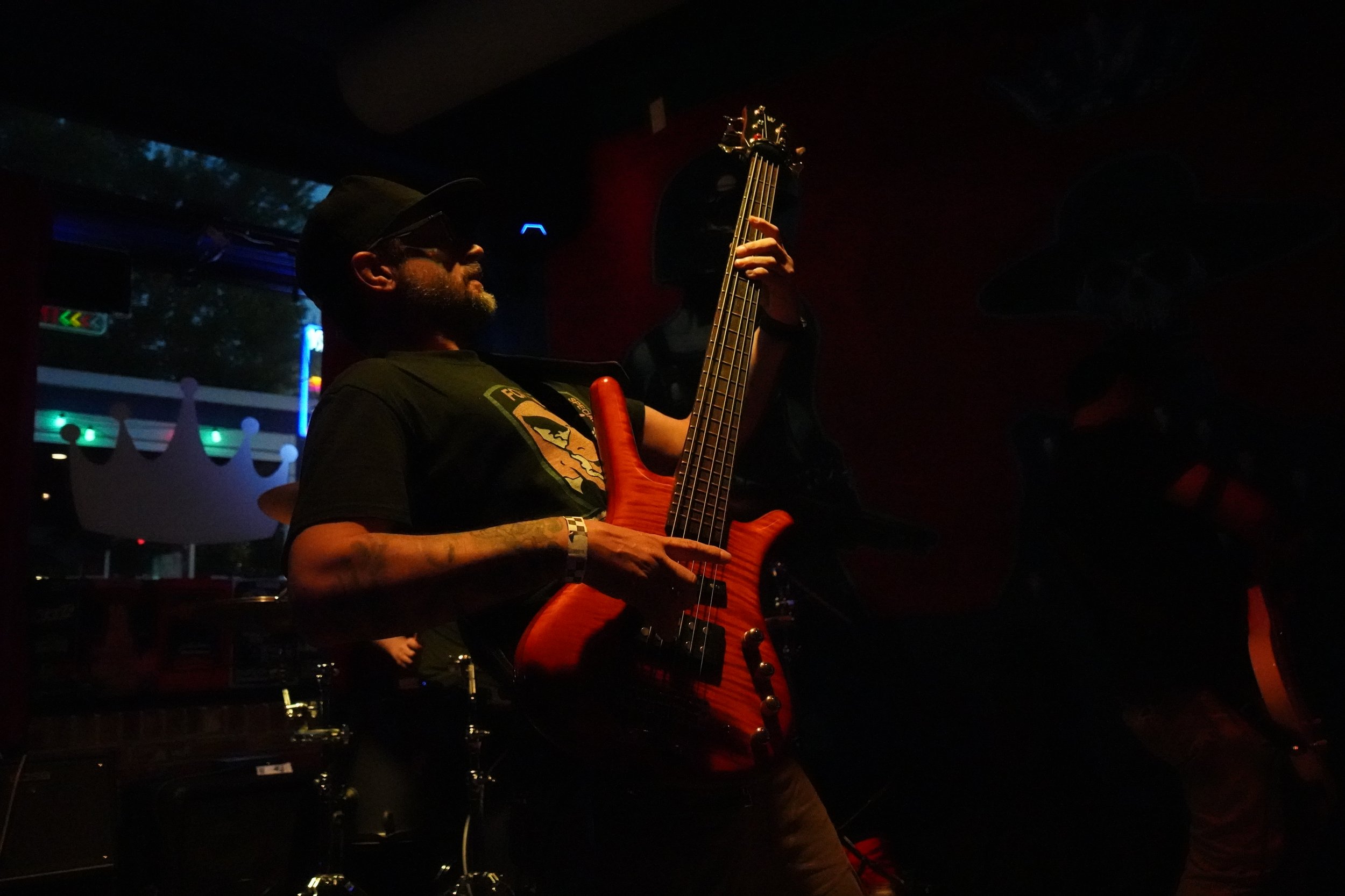 A man playing an electric bass guitar on stage in a dark indoor venue.