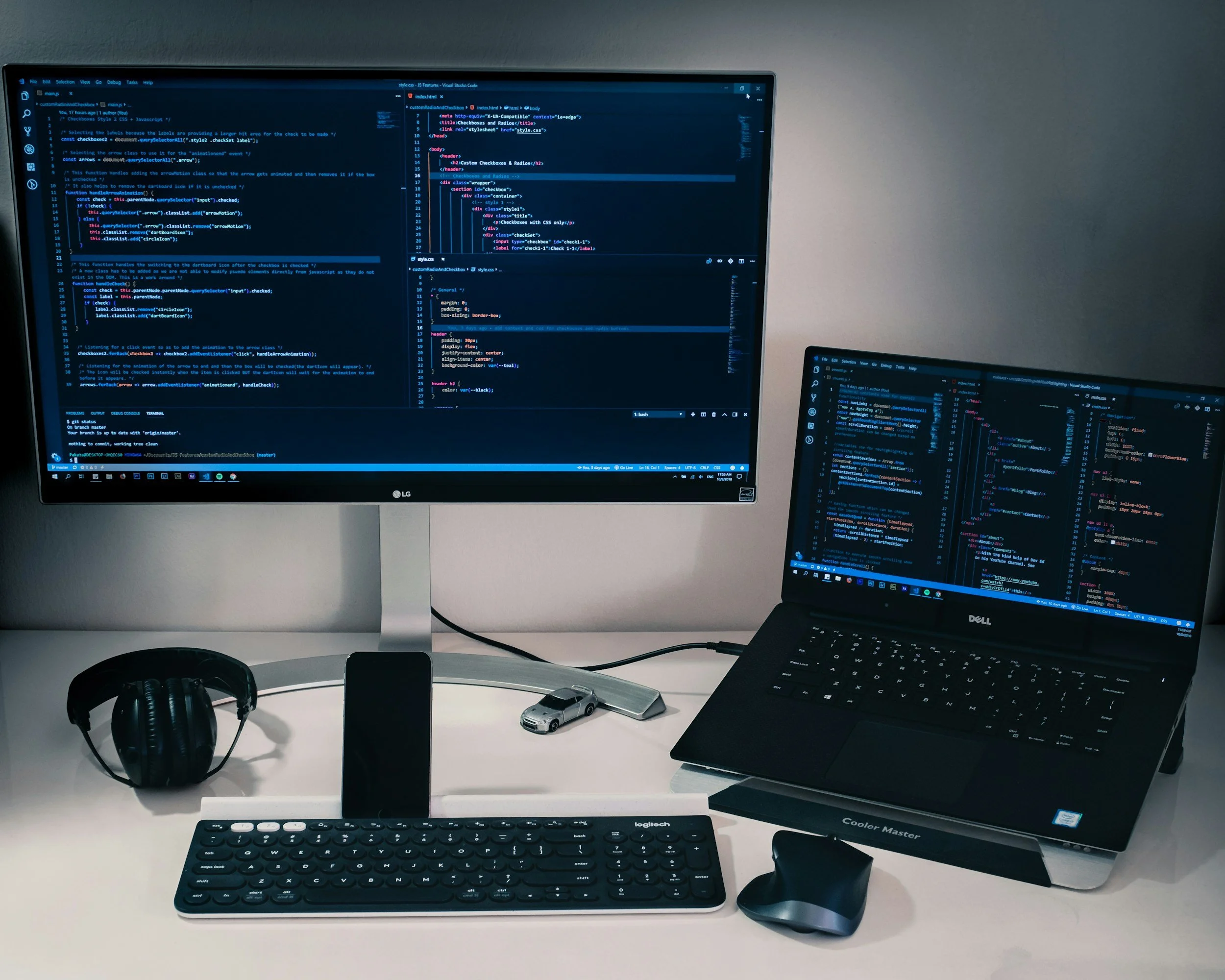 Multiple computer screens displaying code and software development environment, with a white desk that has a keyboard, a mouse, a small toy car, a smartphone, a pair of headphones, and a small remote control.