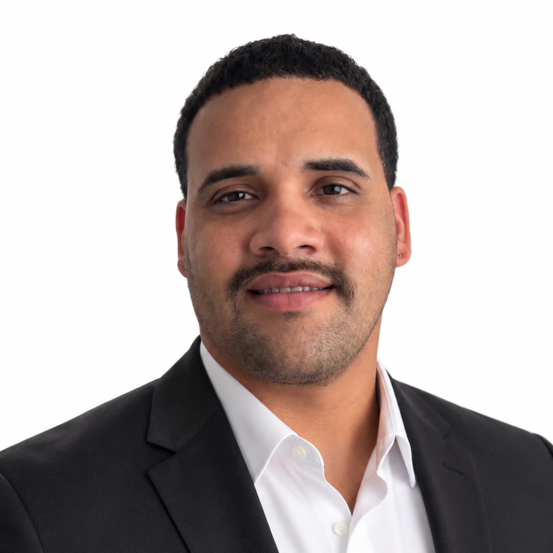 Headshot of a man with dark hair, mustache, wearing a black suit jacket and white shirt, against a plain white background.