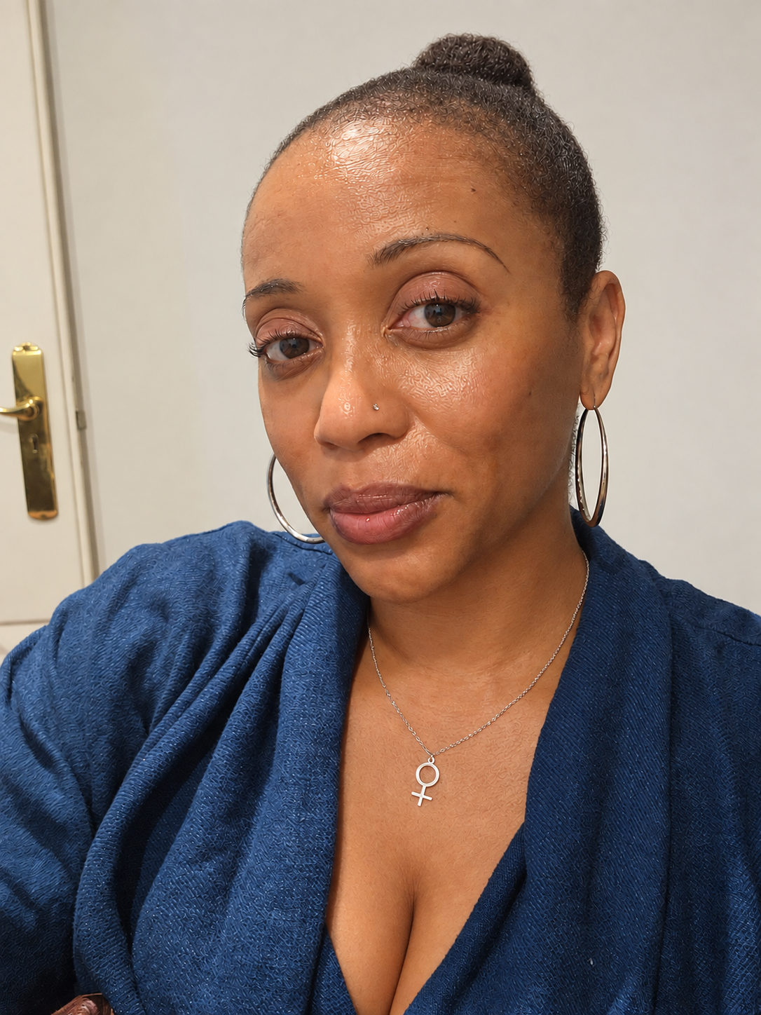Prachel Carter in blue, wearing hoop earrings and a gold pendant.