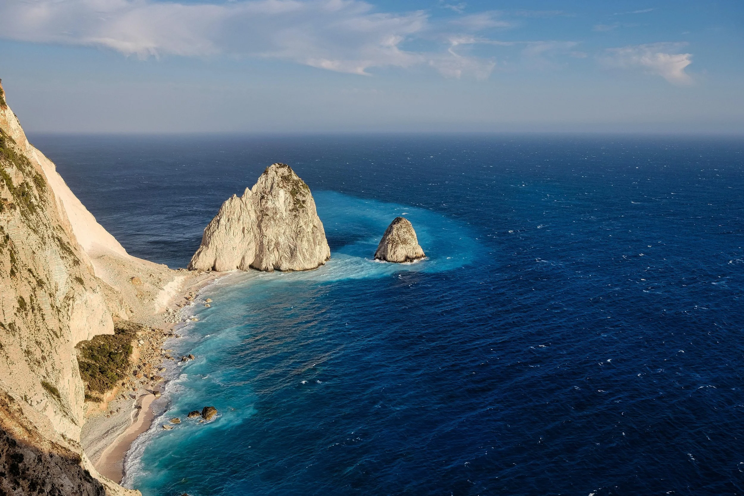 A view of rugged cliffs and rocky formations along a coastline with the ocean extending to the horizon.