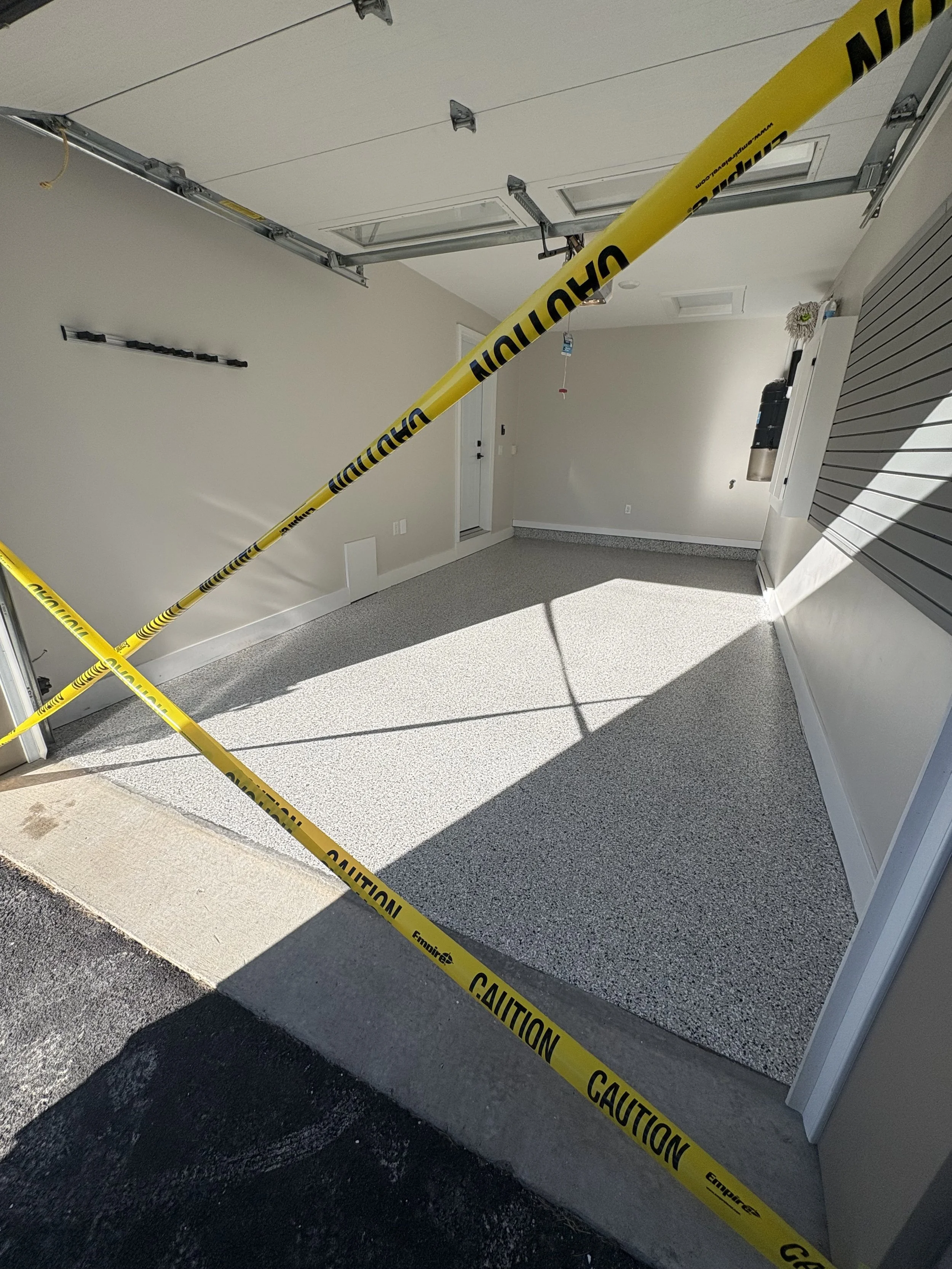 Garage with caution tape across the entrance, open garage door, and sunlight casting shadows.