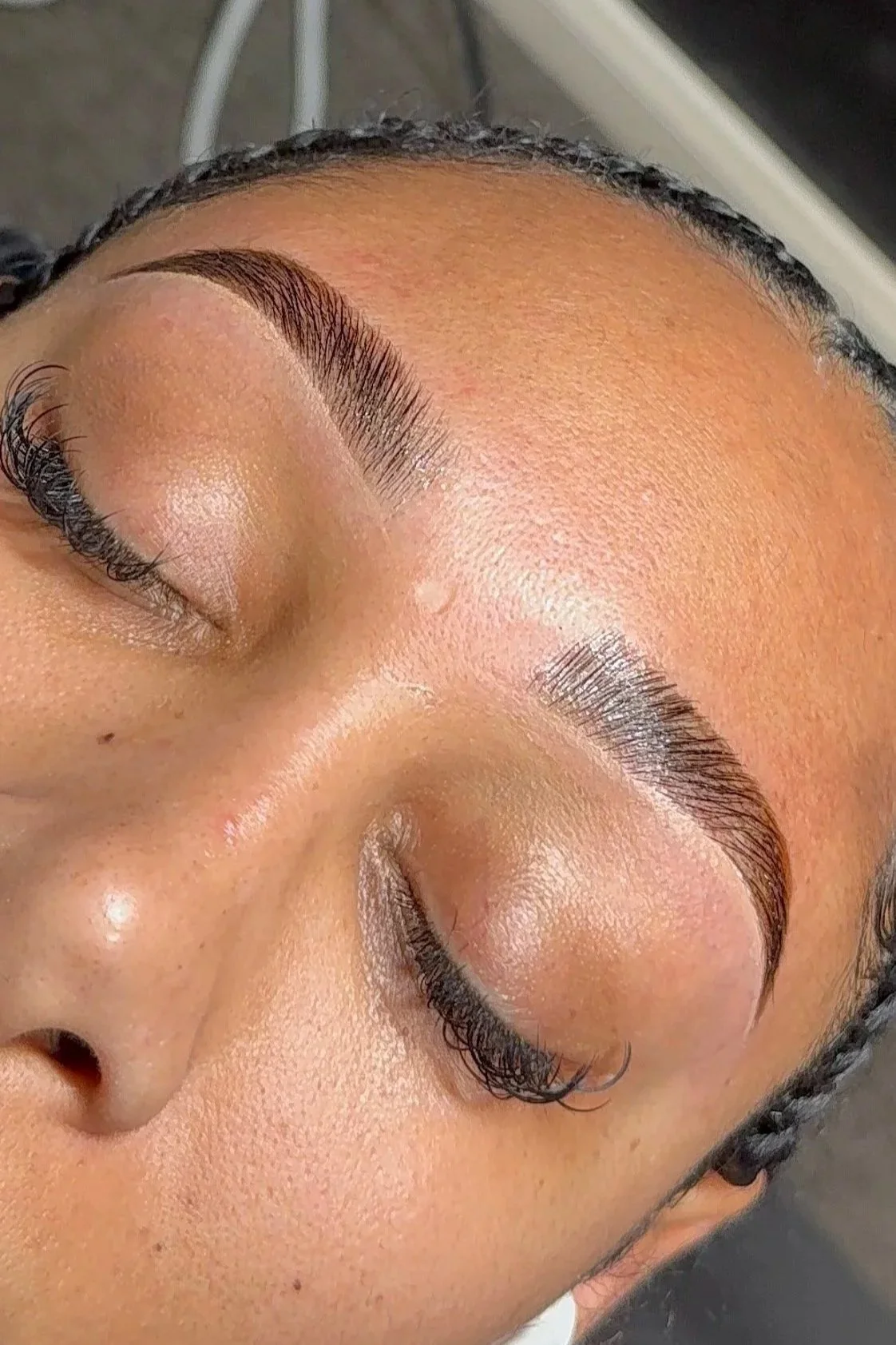 Close-up of a person's face with closed eyes, showing freshly done eyebrow and eyelash enhancements.