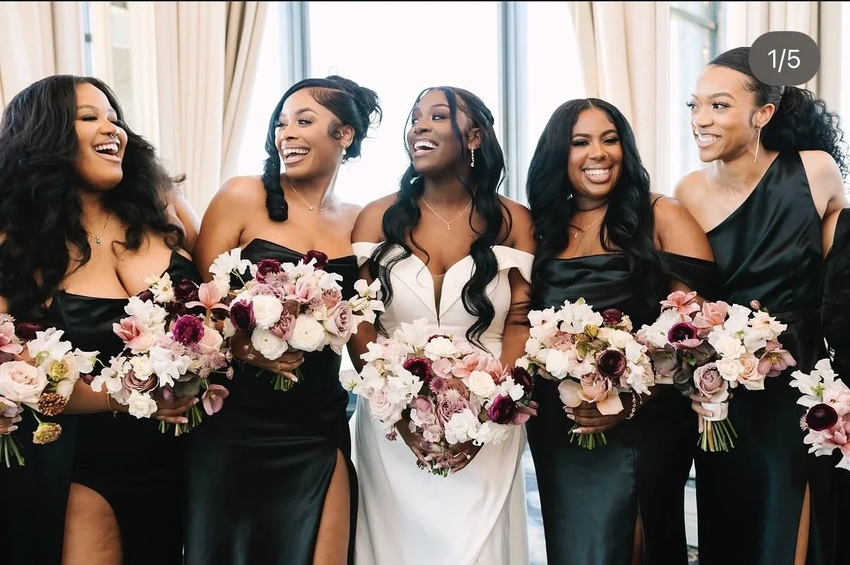 Bride and bridesmaids at a wedding, holding bouquets of flowers, dressed in black and white gowns, smiling and laughing.