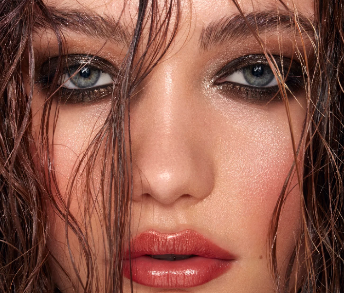 Close-up of a woman's face with wet, wavy hair, blue eyes, and glossy lips.