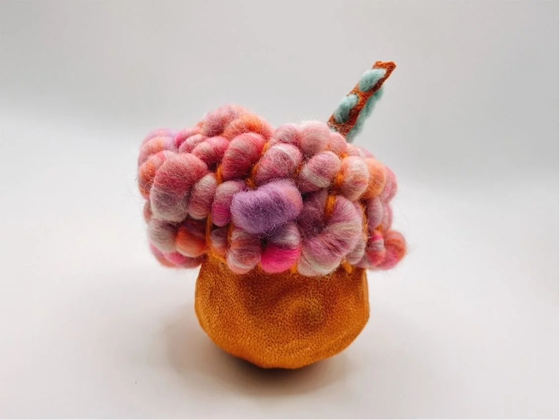 Grapefruit and yarn sculpture. There is a dried grapefruit shell with coached pastel art yarn, a piece of orange peel magically straightened into a thin strip and punched with holes, yarn threaded through. this is one of my 'Crochet Bodies' series.