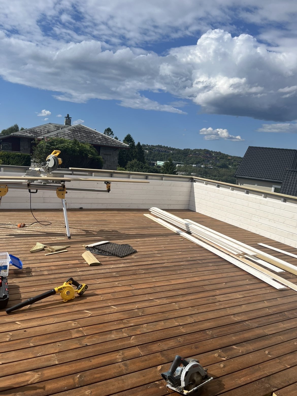 Byggearbeid på terrassen med tremplanker og verktøy under en klar dag med skyer på himmelen.