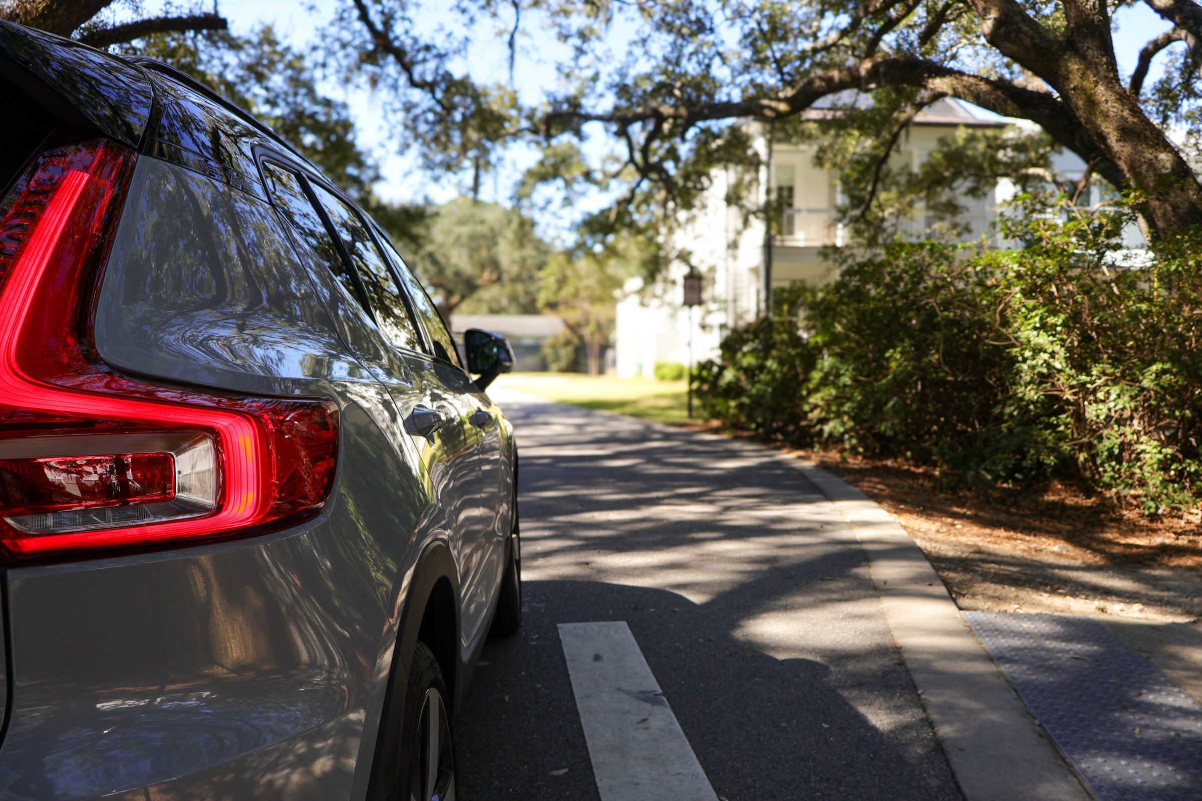 A gray SUV parked beside a sidewalk with trees and a white house in the background.