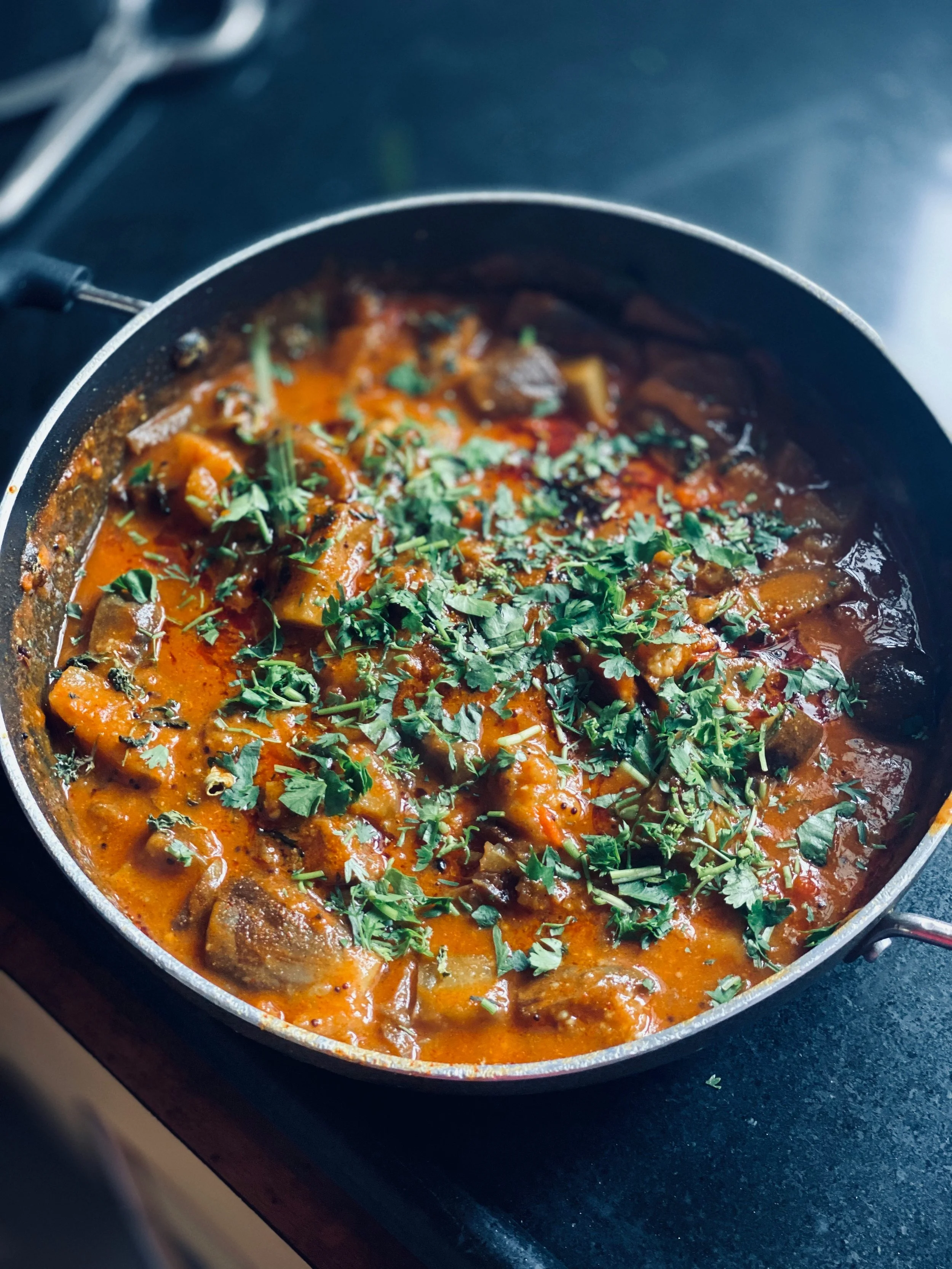 A close-up of a skillet with a stewed dish containing meat, vegetables, tomatoes, herbs, and garnished with fresh cilantro.