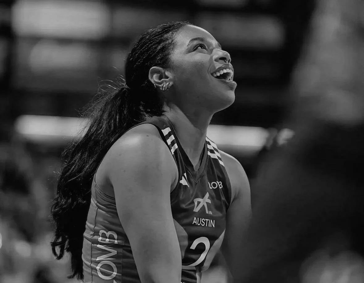 Black and white photo of a female volleyball player smiling, wearing a jersey with the name 'AUSTIN' and the number 2, on an indoor court.