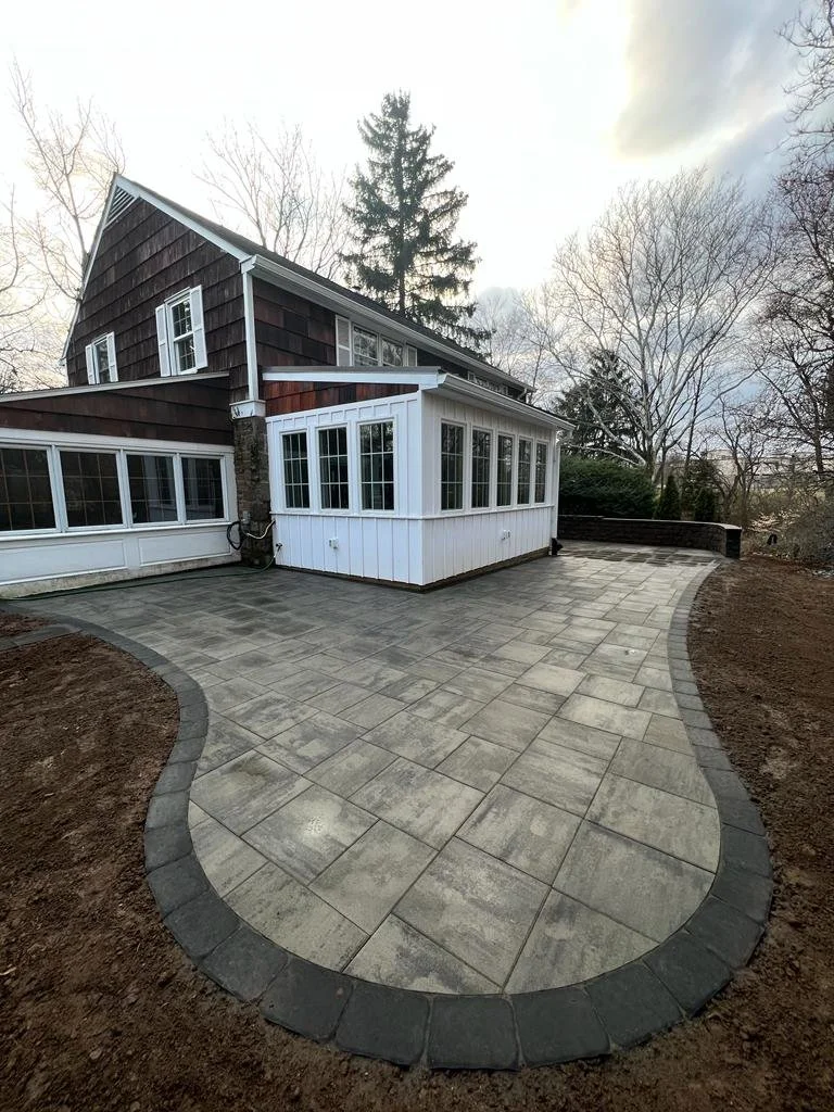 Custom curved patio featuring interlocking pavers, a contrasting border, and a spacious layout that complements the home's rear entrance and surrounding landscape.