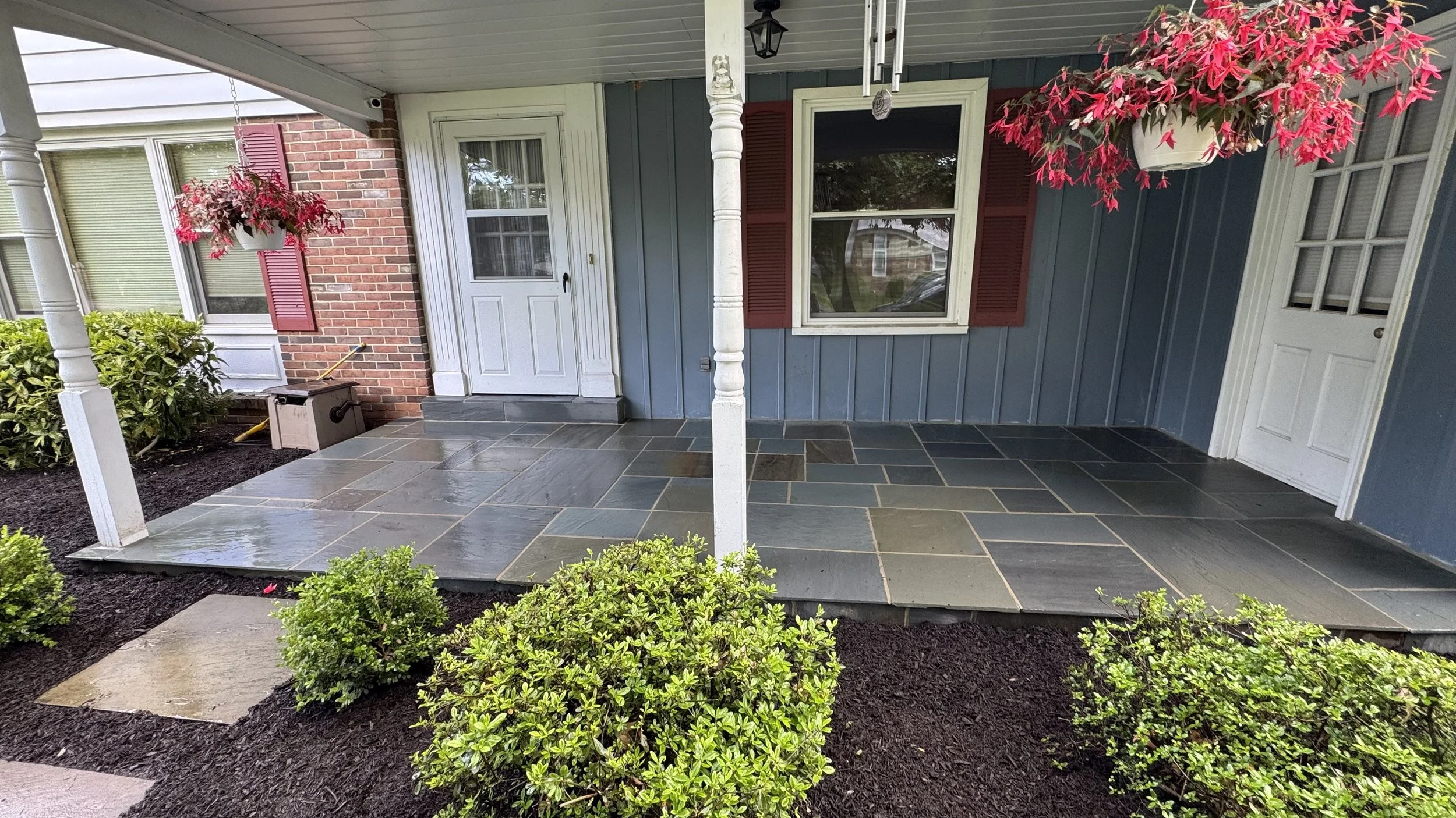 Residential front entrance featuring a paved walkway, covered porch, and neatly maintained ornamental shrubs that complement the home's exterior.