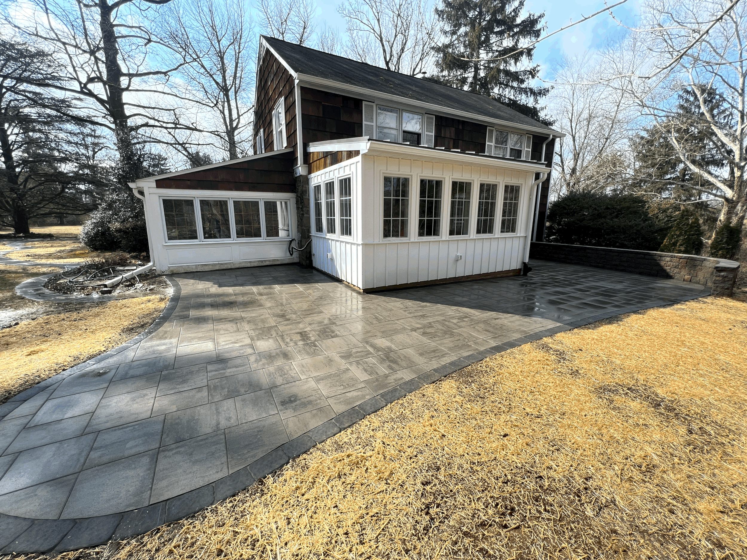 Spacious residential hardscape area featuring a paved outdoor surface surrounding an enclosed porch, creating a functional space for outdoor living.