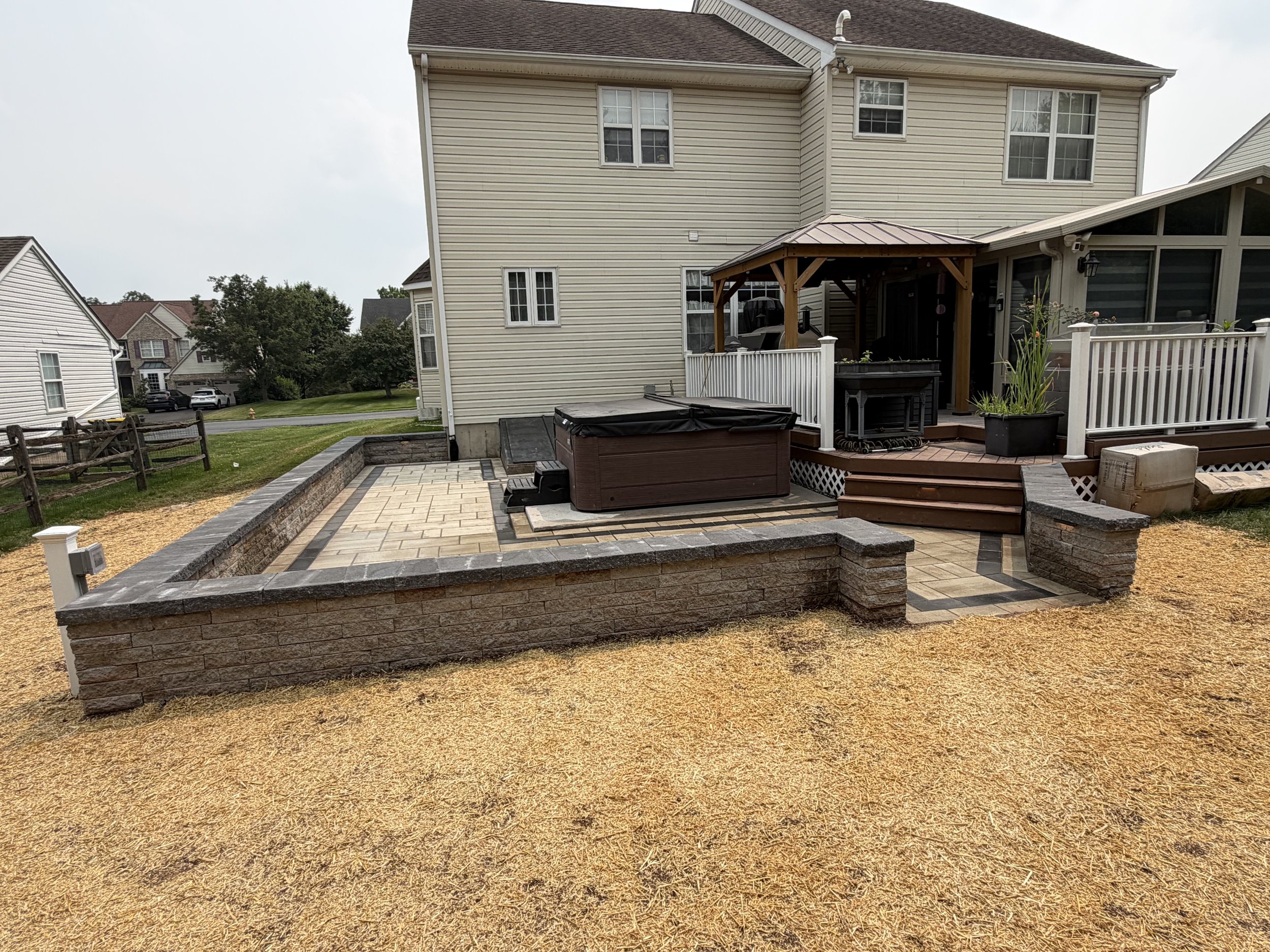 Custom retaining wall installation using decorative concrete blocks to support an elevated patio, featuring integrated stone steps and a durable design that enhances the backyard landscape.