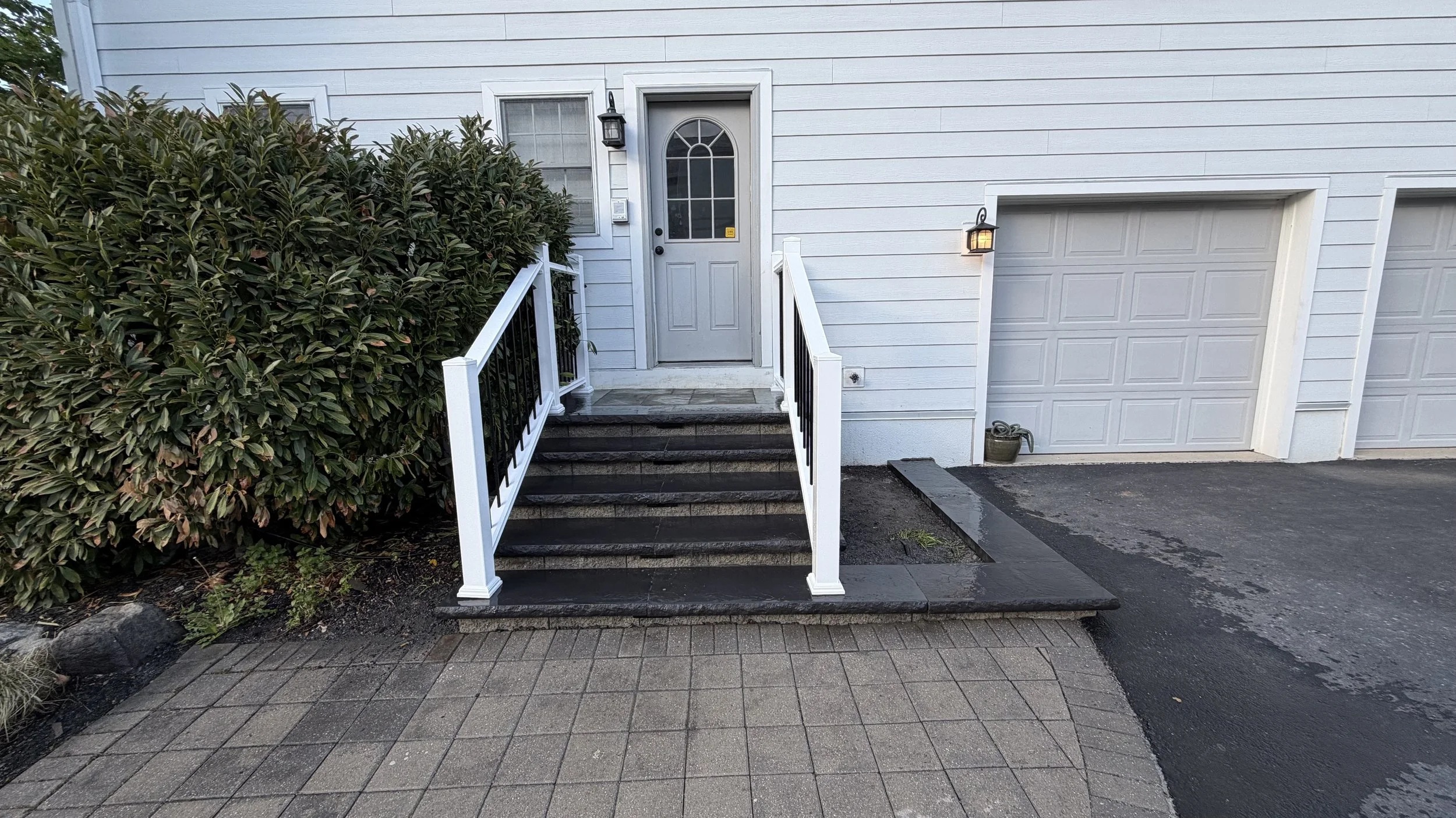 Residential front entrance featuring exterior steps, white handrails, and a paved landing that provides access to the home's main doorway.