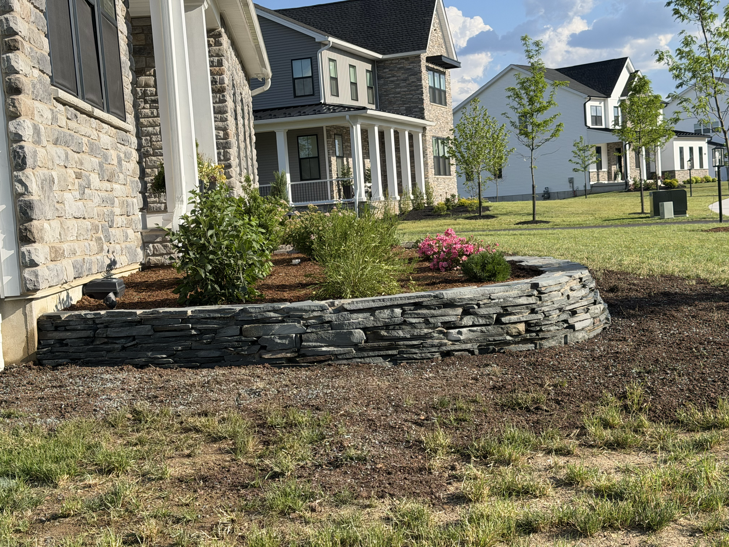 Residential foundation landscaping featuring low-growing shrubs, ornamental plants, and defined garden beds designed to complement the home's front porch.