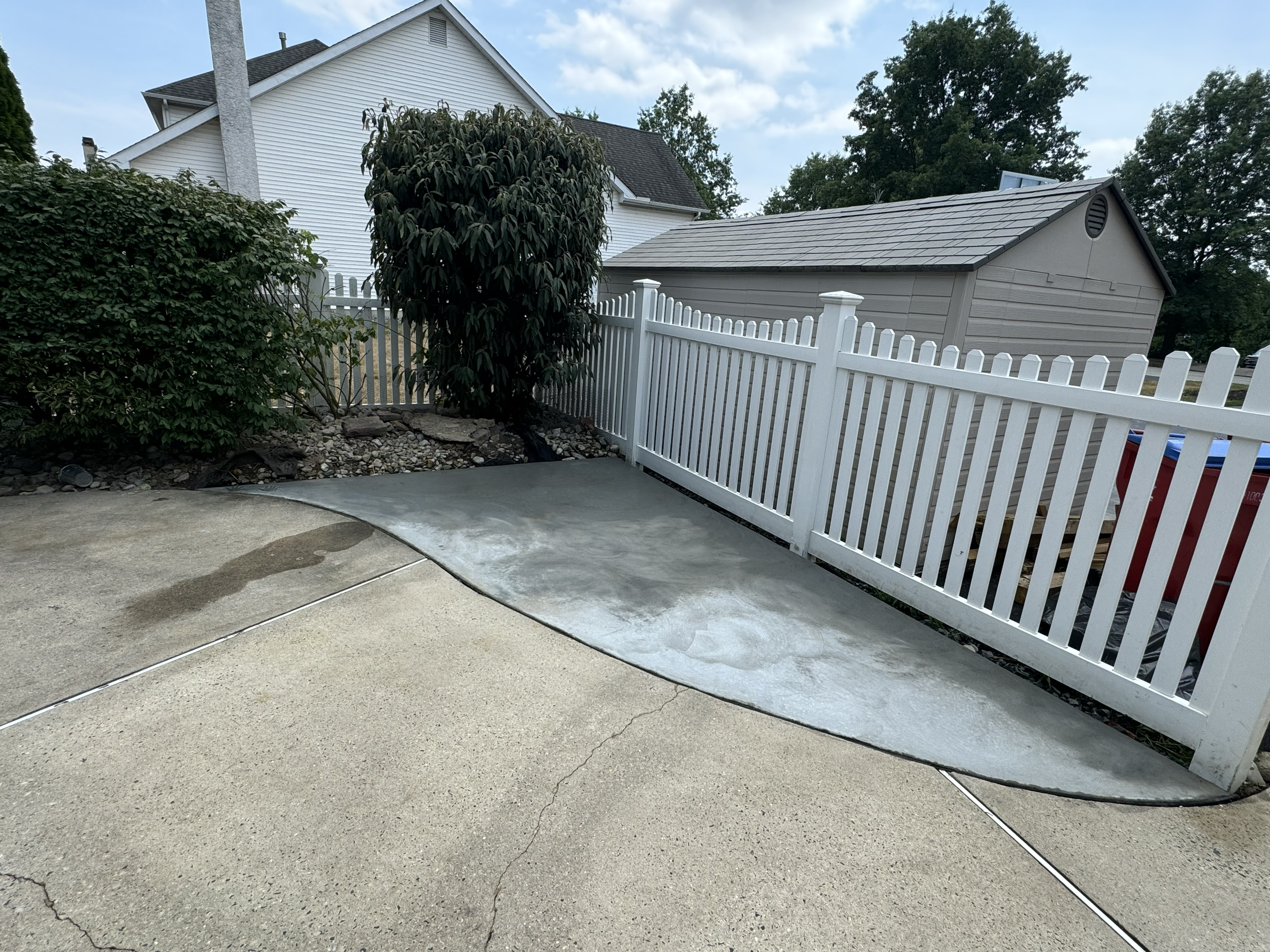 Concrete slab installation featuring a rectangular paved surface, straight edges, and a smooth finish, creating a functional outdoor area between landscaped garden beds.