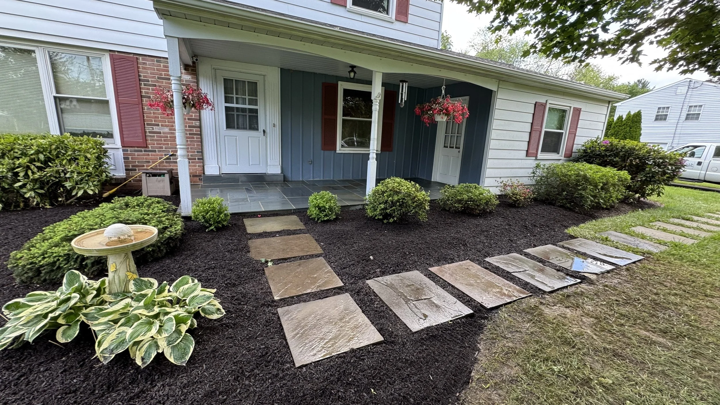 Front entrance landscaping featuring square stepping stones set in dark mulch, ornamental shrubs, and neatly defined planting beds that complement the home's covered porch.