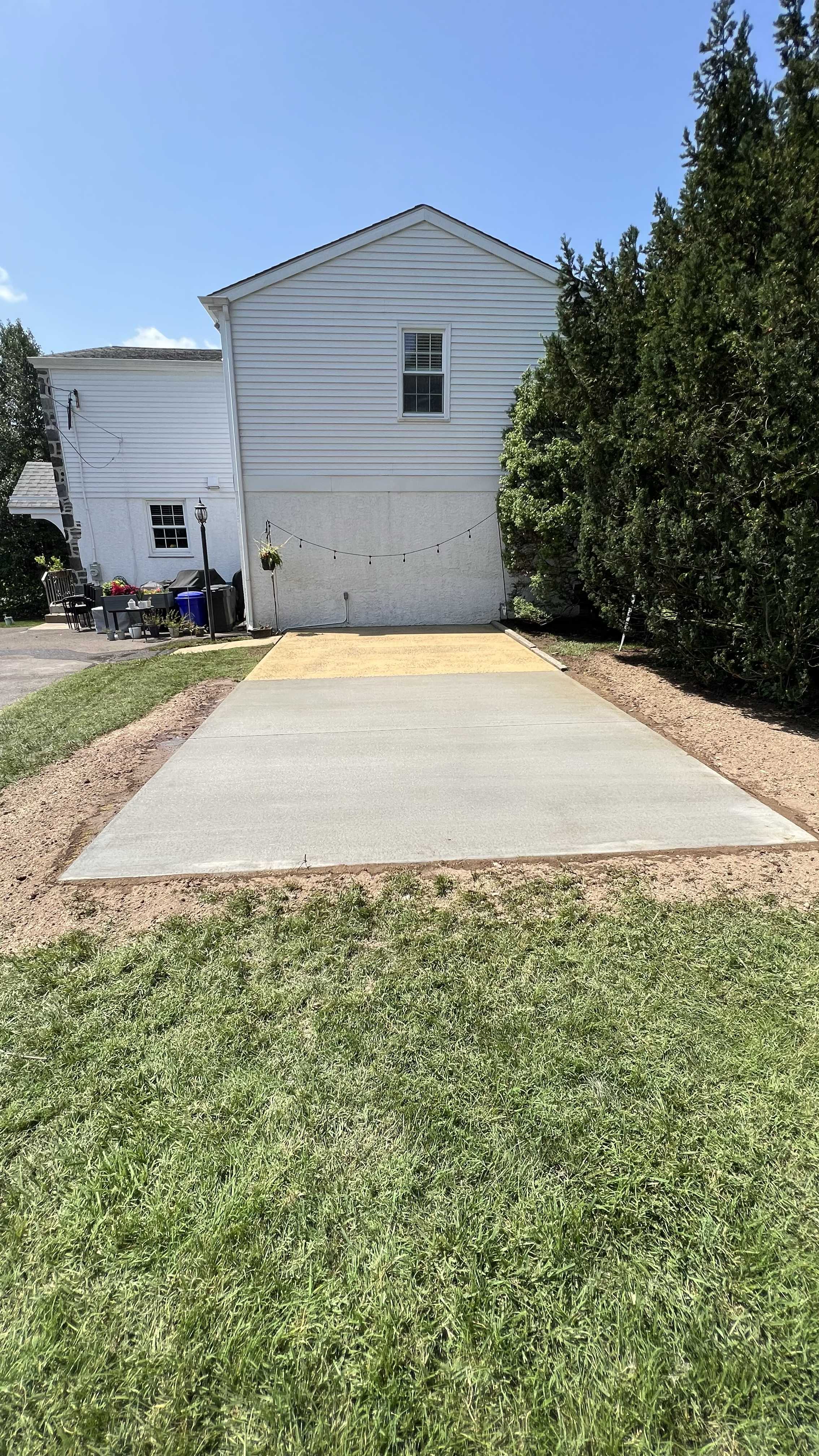 Concrete slab installation featuring a rectangular paved surface, straight edges, and a smooth finish, creating a functional outdoor area between landscaped garden beds.