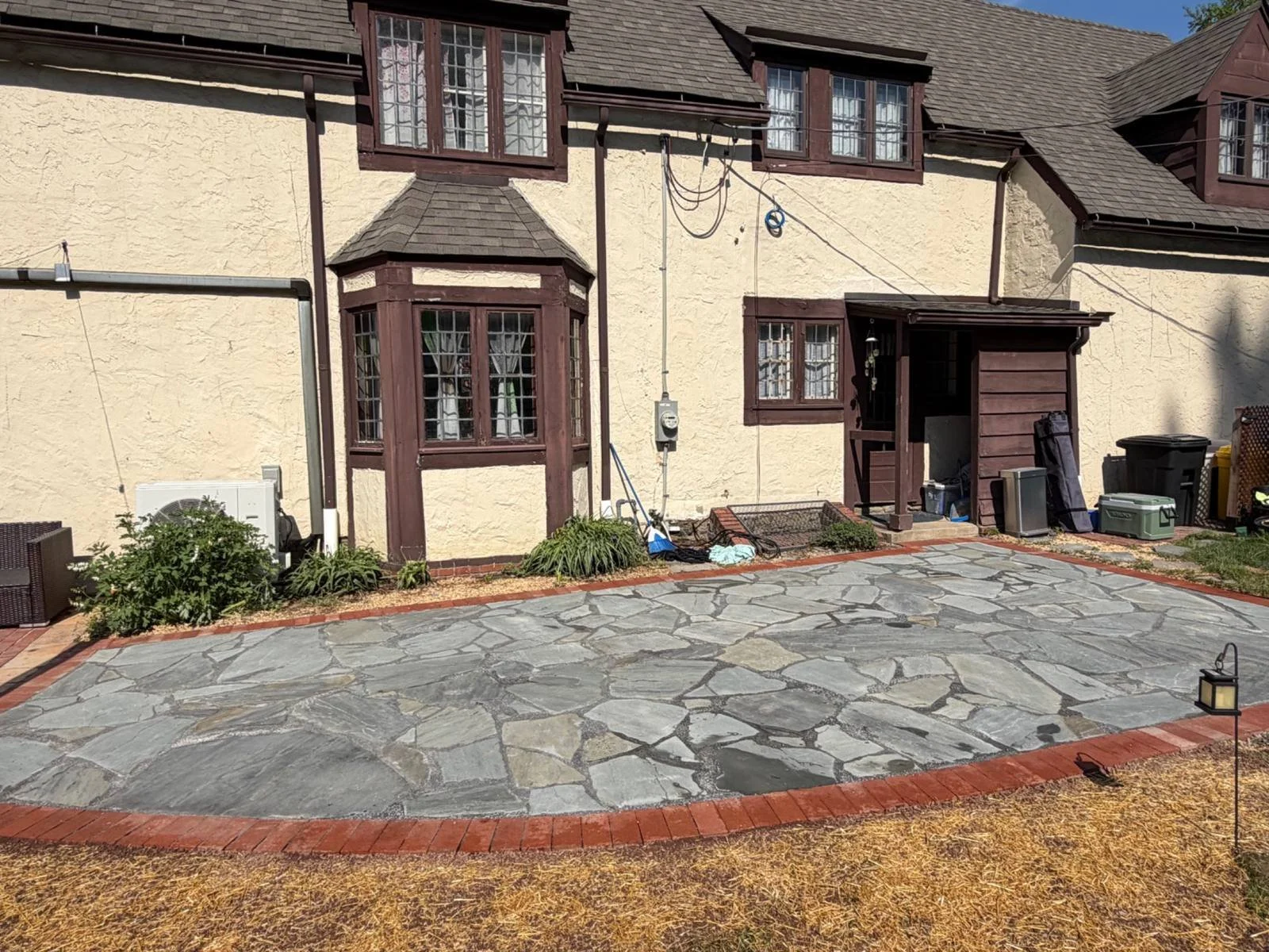 Residential front entrance featuring a spacious decorative flagstone surface with a contrasting brick border, complementing the home's exterior and surrounding landscape.