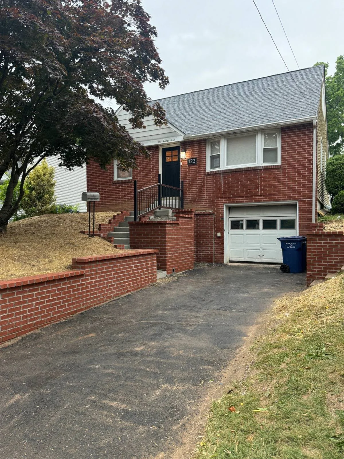 Residential landscape retaining wall featuring decorative masonry construction alongside a driveway and entrance steps, helping define the elevated landscape and complement the home's exterior.