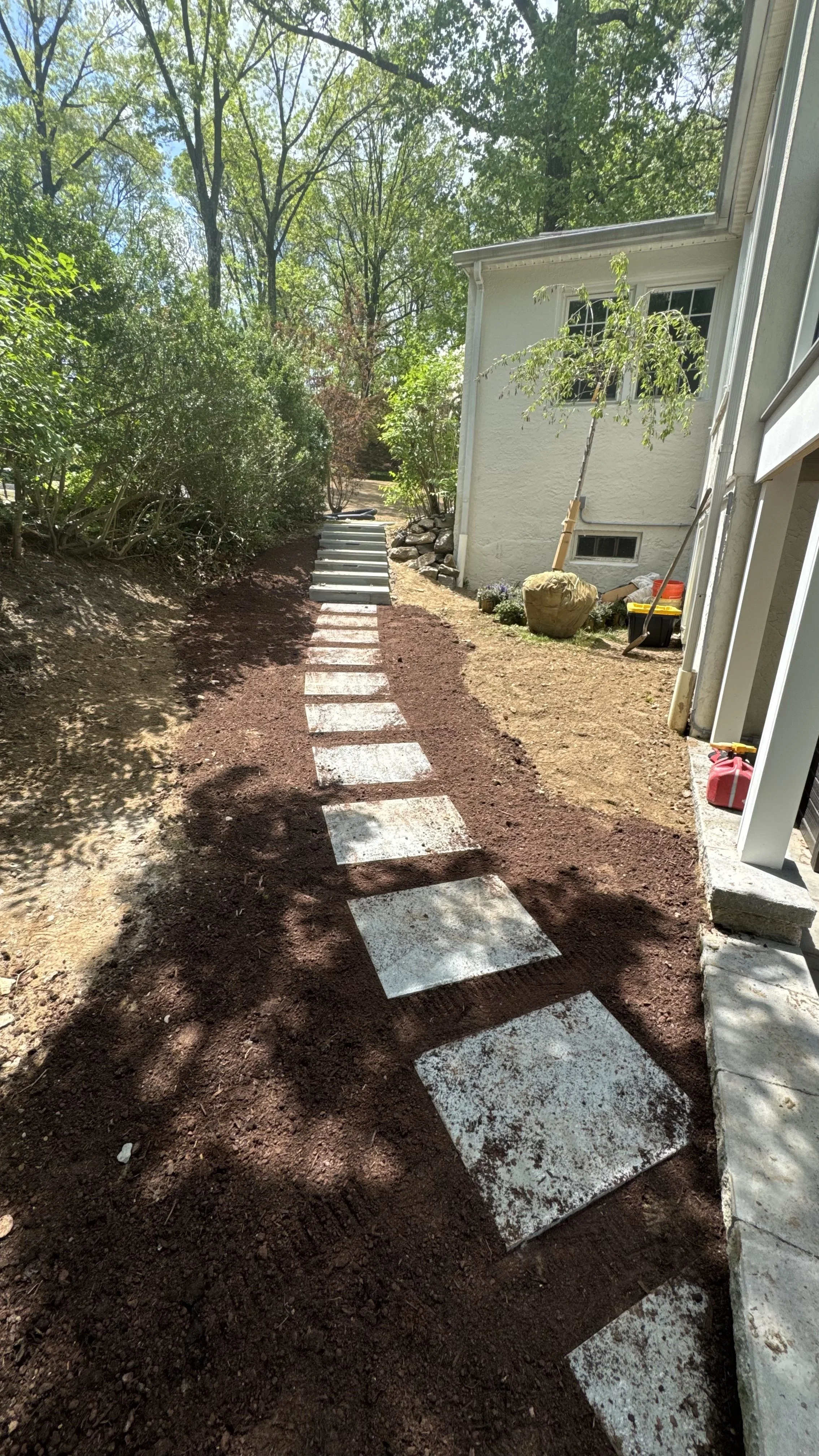 Garden walkway featuring individual natural stone stepping stones set through a mulched landscape bed, providing a practical path along the side of a home.
