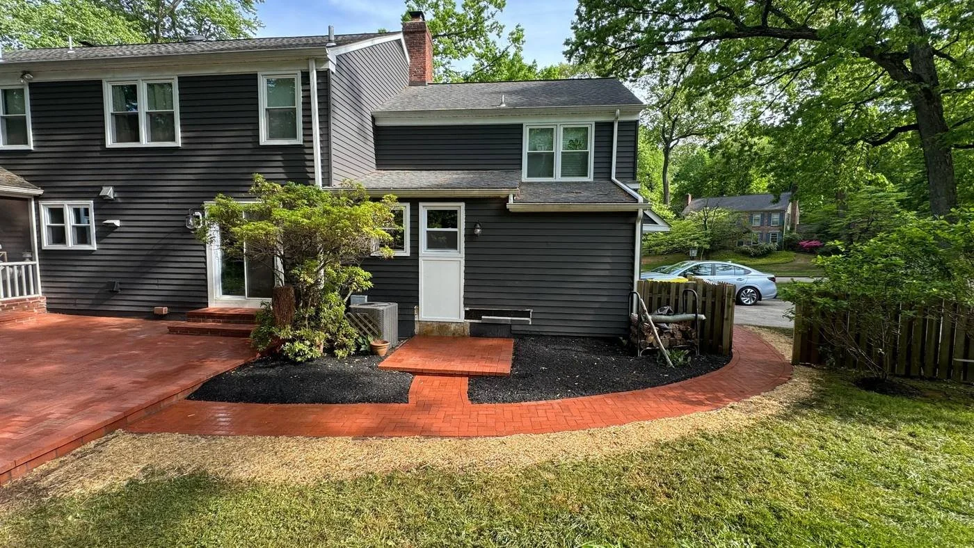 Custom red brick paver patio and curved walkway installed around a residential home.