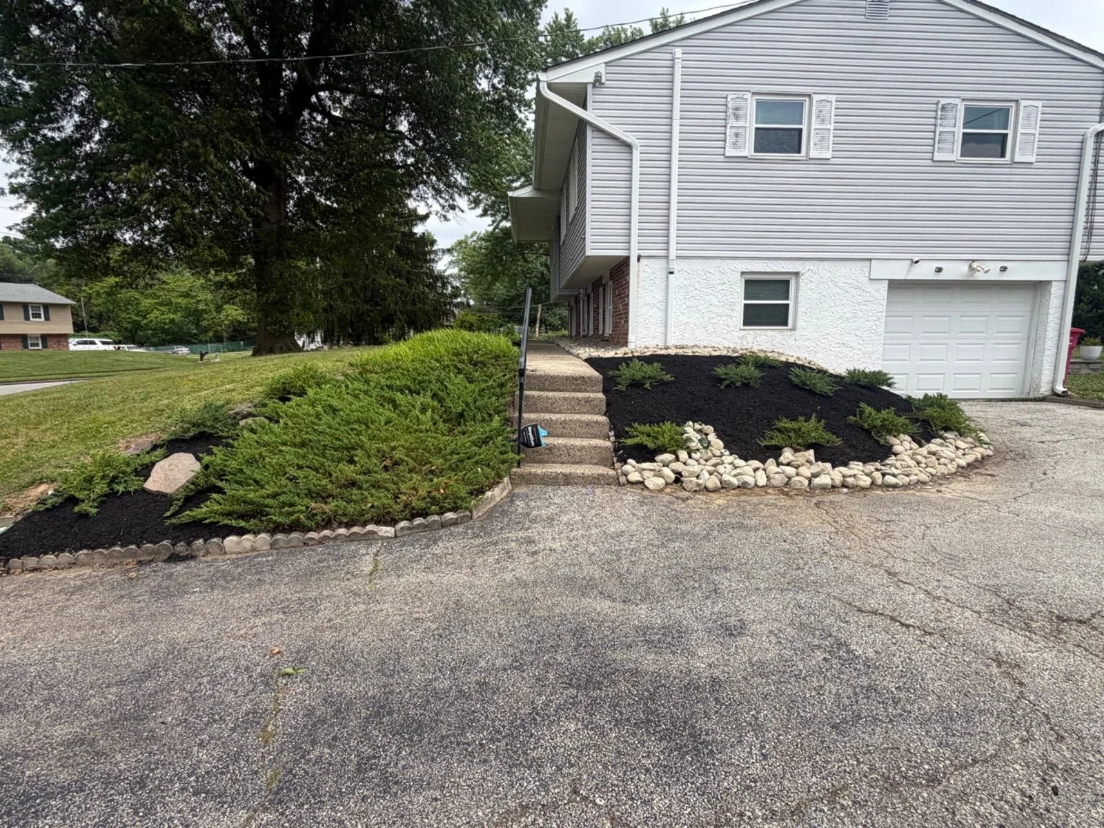 Residential landscaping featuring neatly shaped evergreen shrubs, defined planting beds, and decorative white stone accents along the driveway and front entrance.
