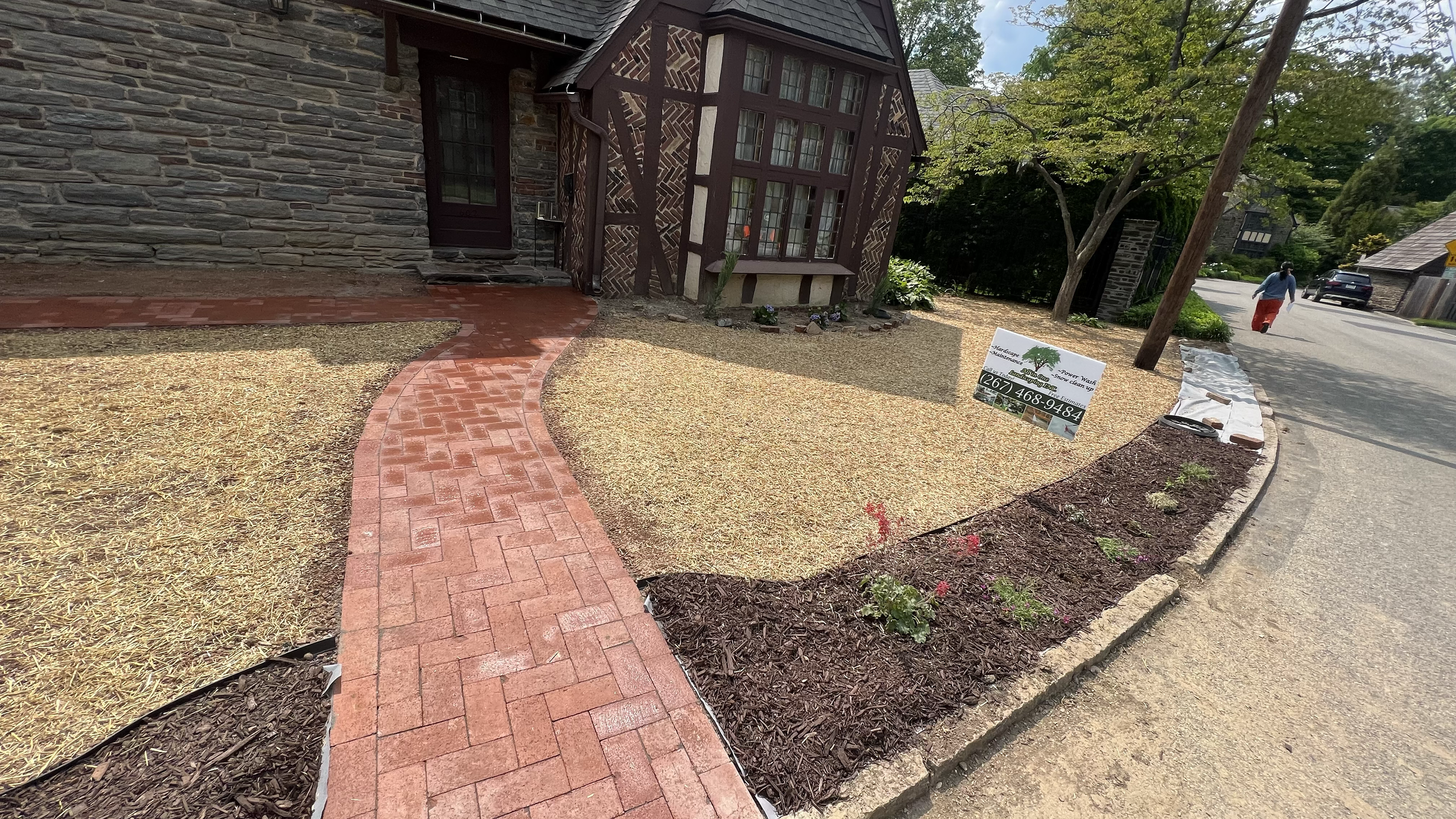 Curved red brick walkway alongside a residential home, featuring decorative stone edging, mulched planting areas, and a landscaped entrance with a traditional finish.