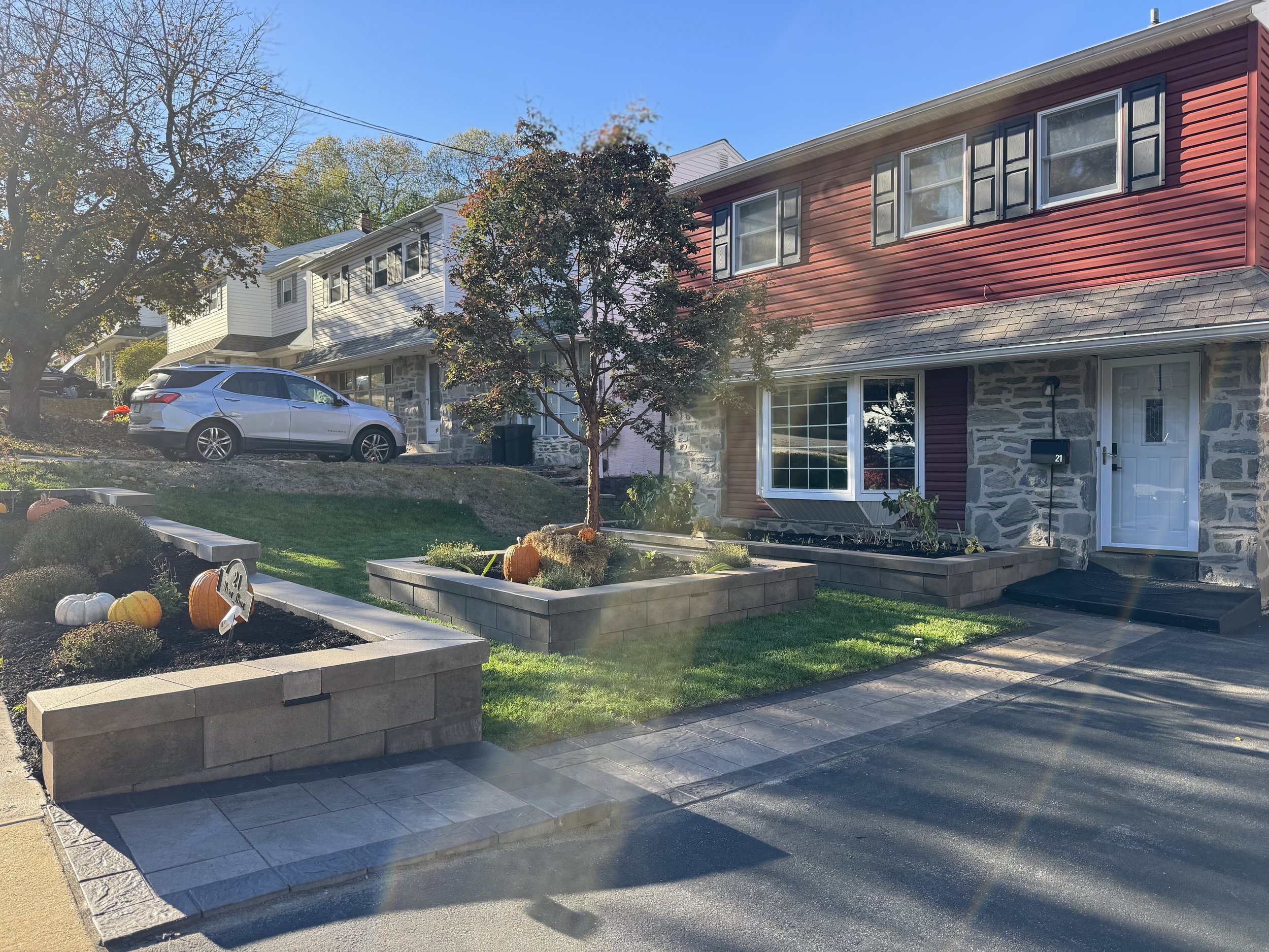 Raised landscape bed supported by a natural stone retaining wall, featuring colorful ornamental plants and layered greenery near the front of a home.
