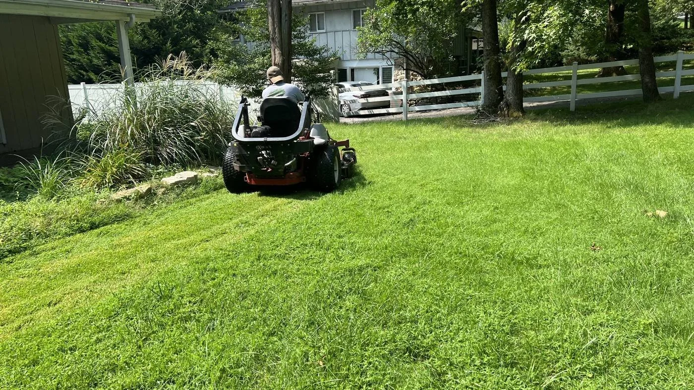 Professional landscaper mowing a residential lawn with a zero-turn mower as part of lawn care and landscape maintenance services.