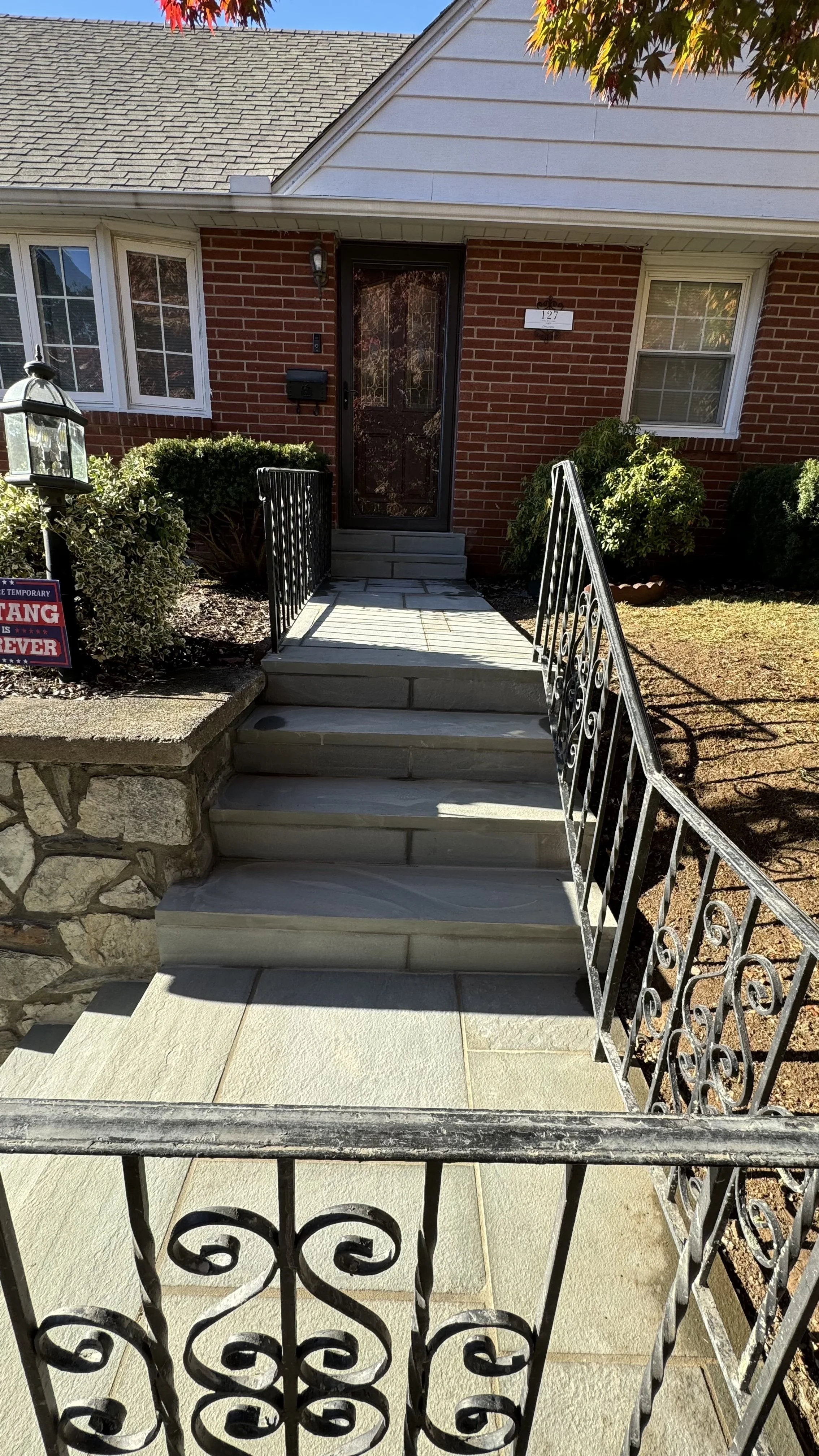 Residential entry staircase featuring stone steps, masonry sidewalls, and decorative black metal railings that complement the home's brick exterior.
