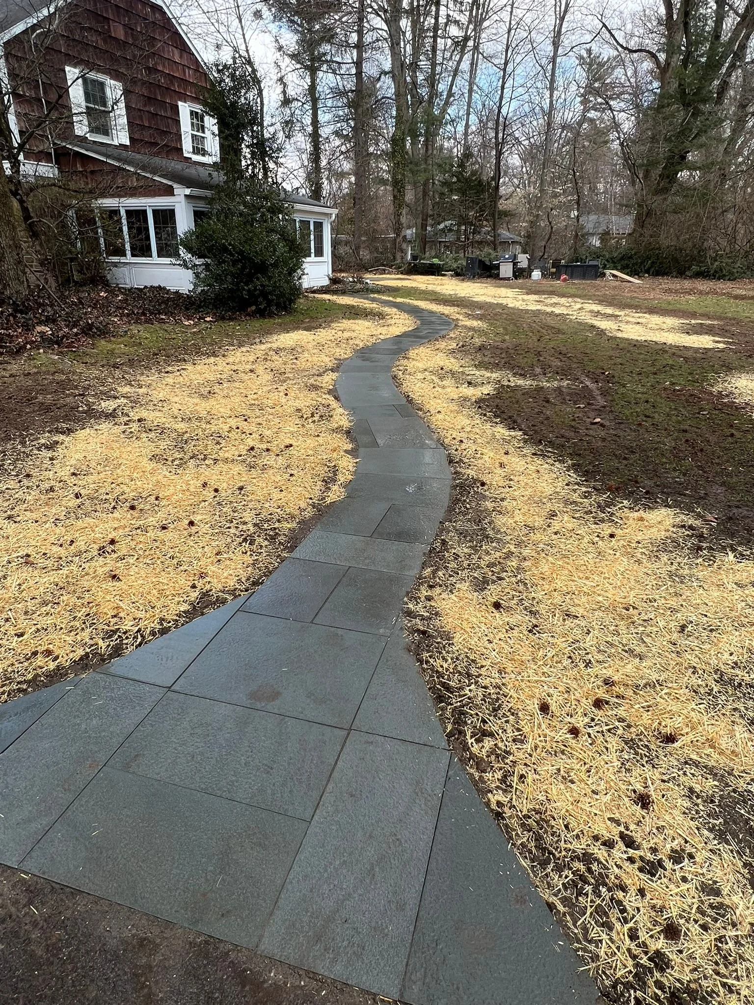 Curved flagstone pathway winding through a residential yard, with surrounding soil and grass areas prepared for landscape restoration.