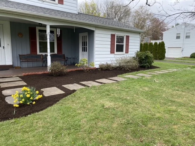Front yard landscaping featuring fresh dark brown mulch, decorative steppingstones, flowering plants, and neatly maintained garden beds that enhance the home's curb appeal.