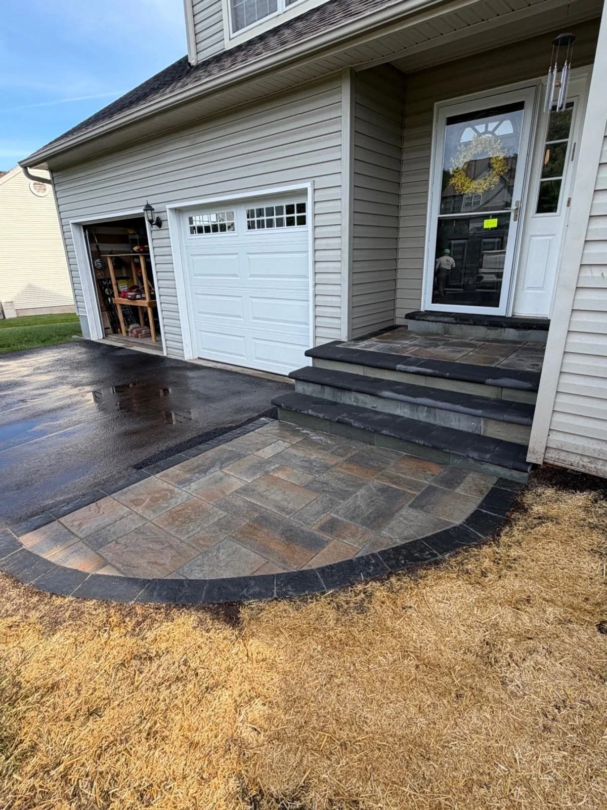 Residential garage entrance featuring a custom paver apron with a curved design and contrasting border, creating a defined transition between the driveway and garage.