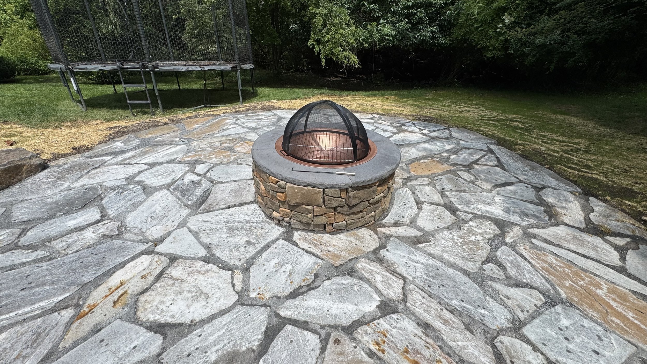 Custom outdoor fire pit surrounded by irregular natural stone paving, creating a distinctive gathering area for backyard entertaining and relaxation.